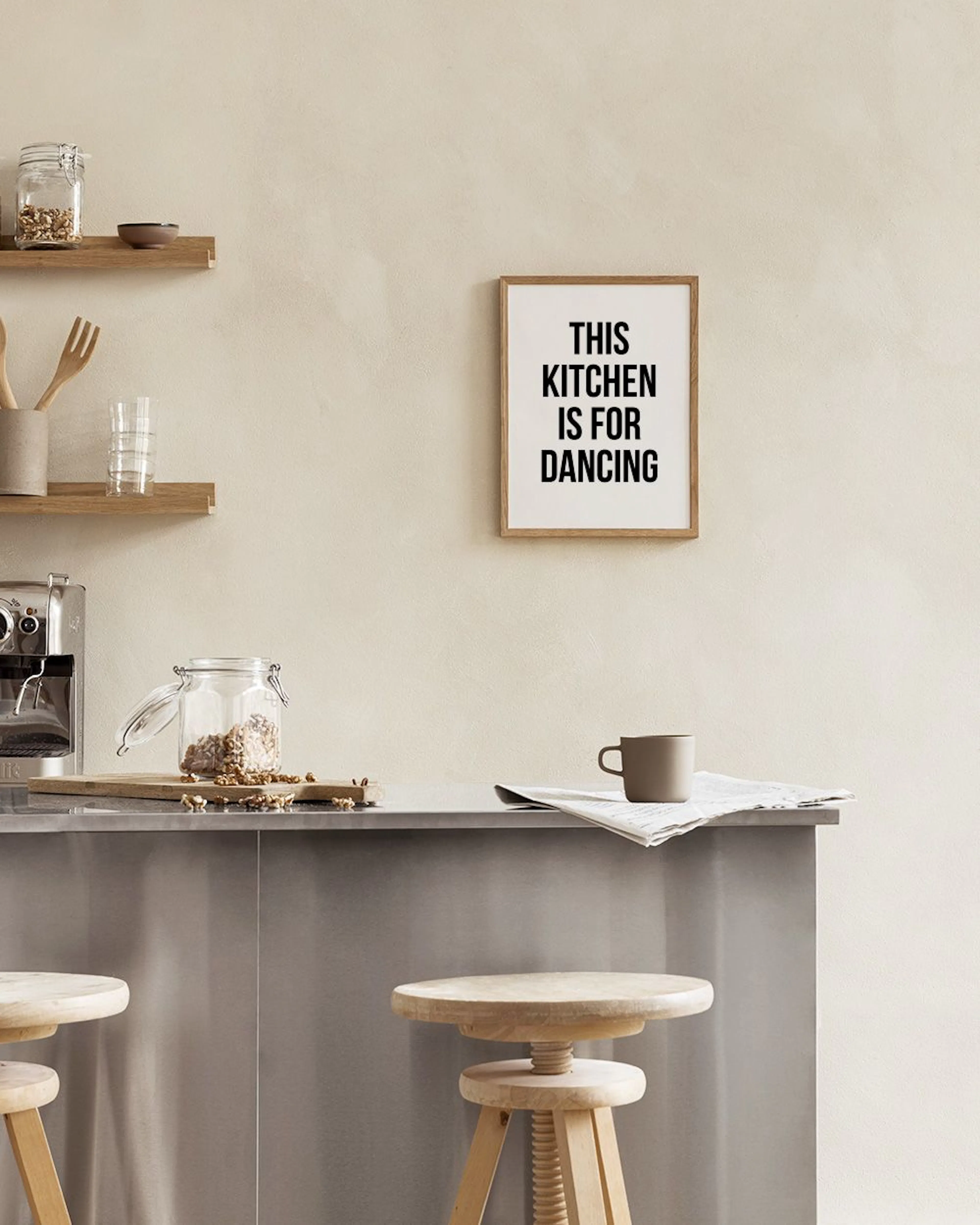 A print with THIS KITCHEN IS FOR DANCING text in a gold frame, displayed on a white marble wall with kitchen accessories.