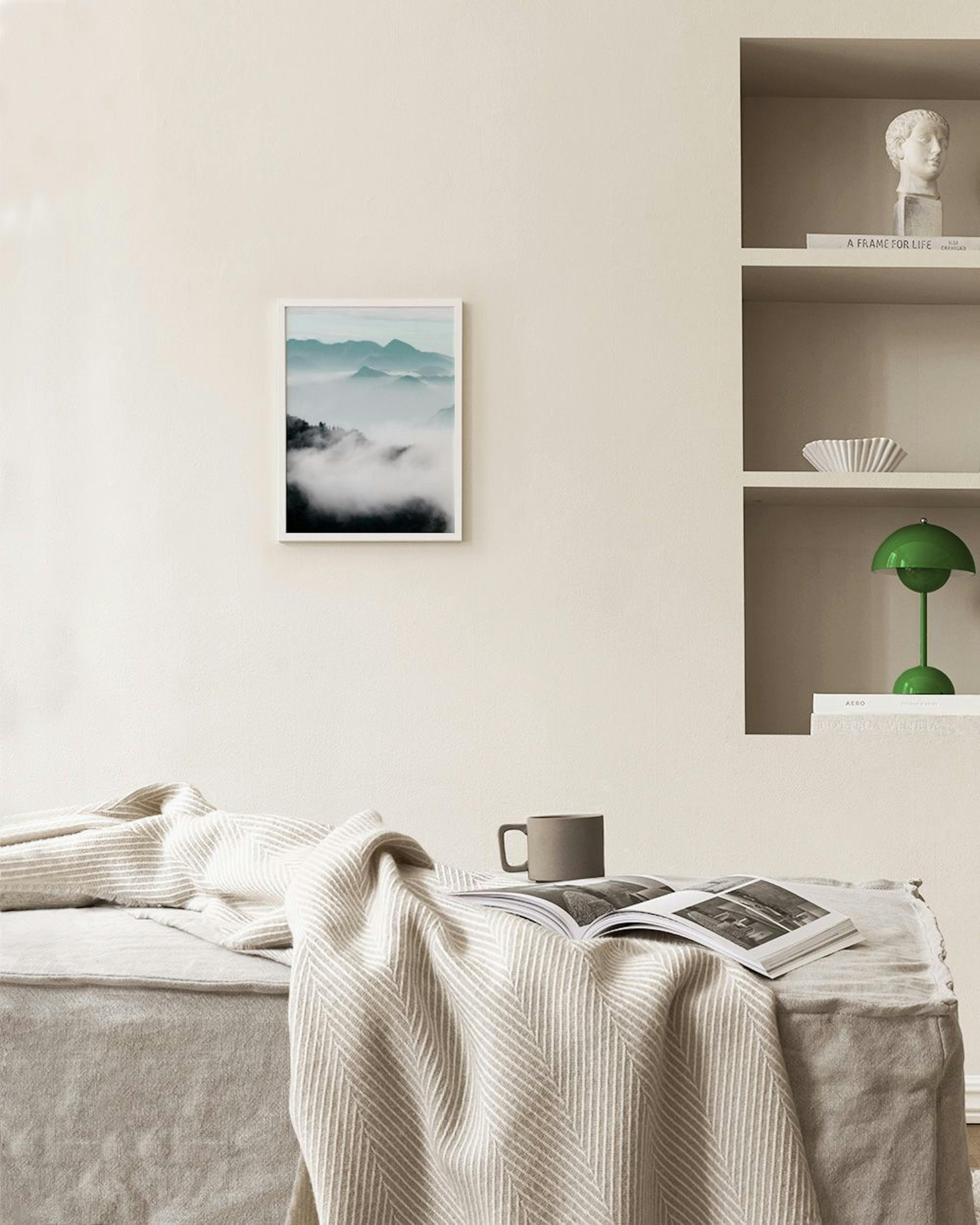 A print of misty mountains and clouds in shades of grey and white, hanging on a dark grey wall above an industrial style lamp.