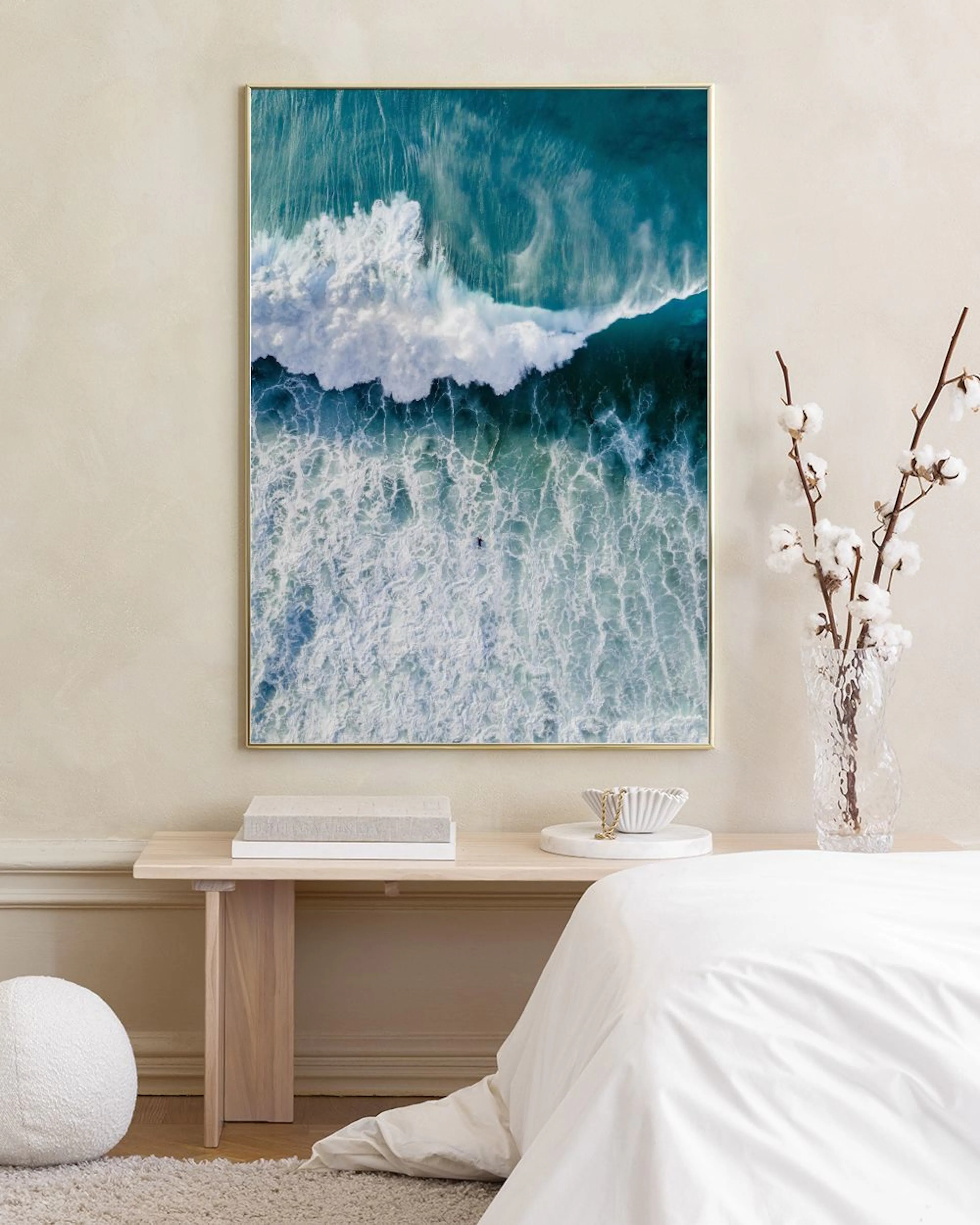 Poster van hoge golven met schuimende witte toppen, hangend boven een wit dressoir met een ronde vaas en naast een donkere stoel