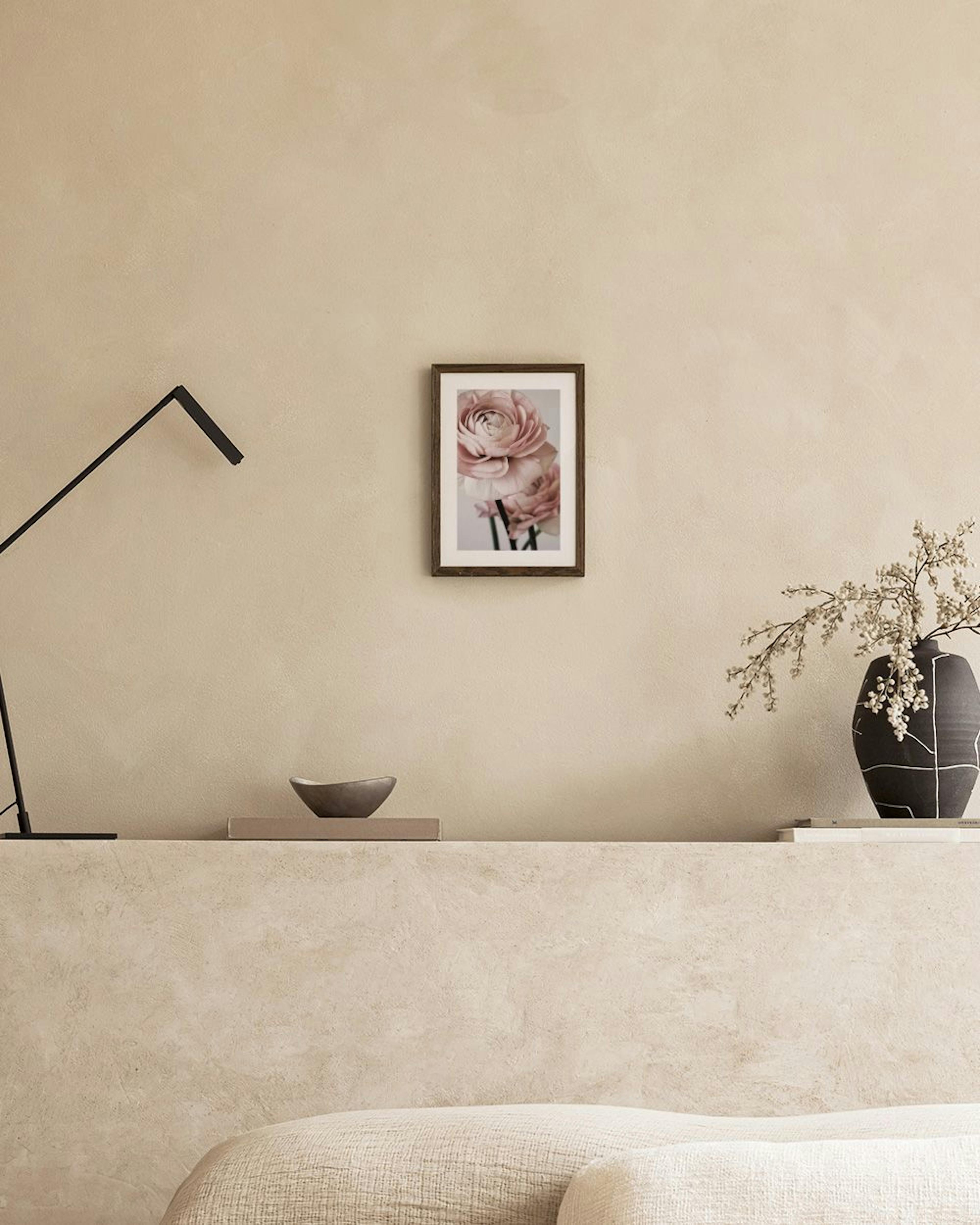 A floral print of light pink ranunculus flowers displayed above a dark red cabinet with a vase and flowering branch.