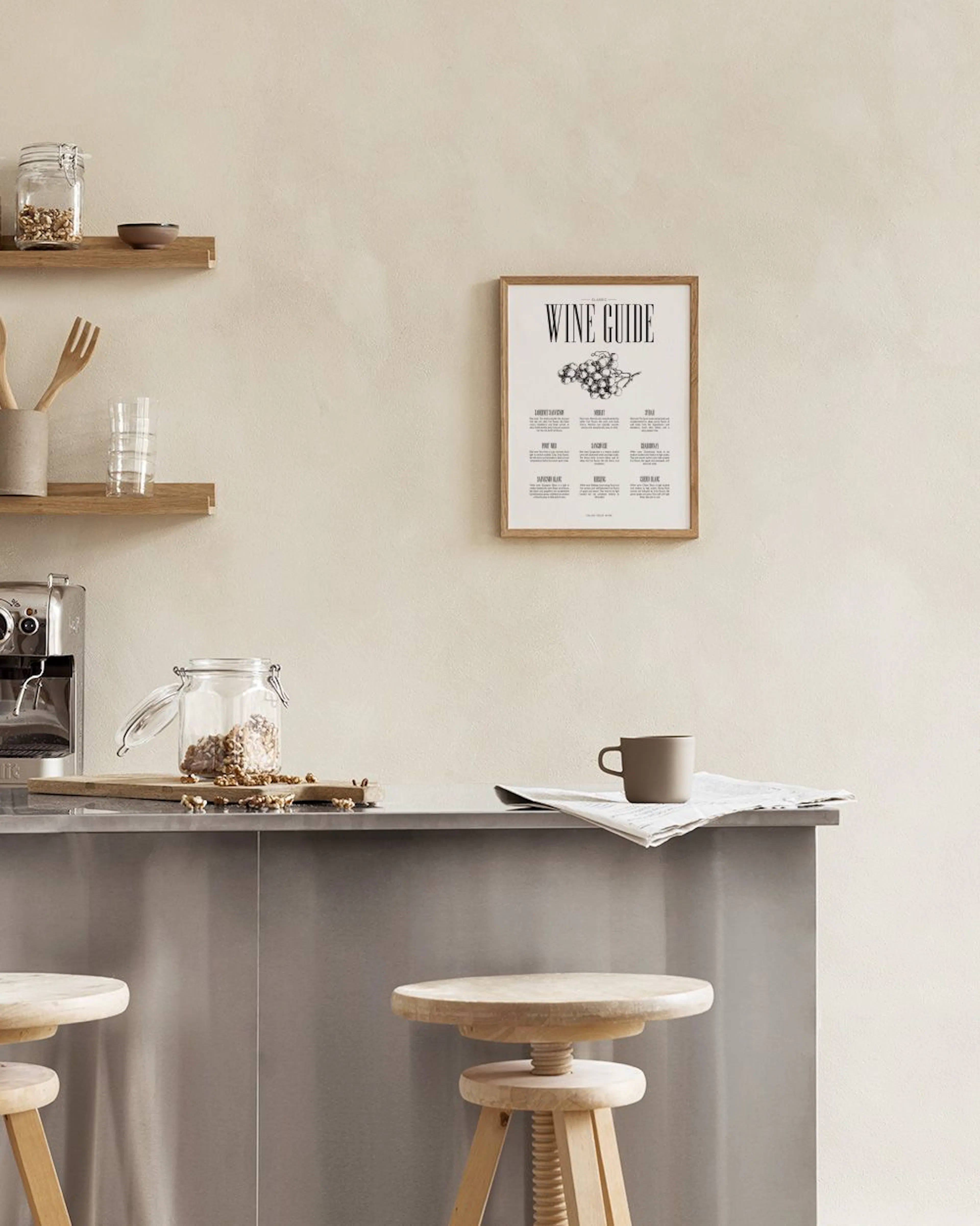 A wine guide print with a grape illustration, displayed on a counter with various kitchen items and a plant in a cloche.