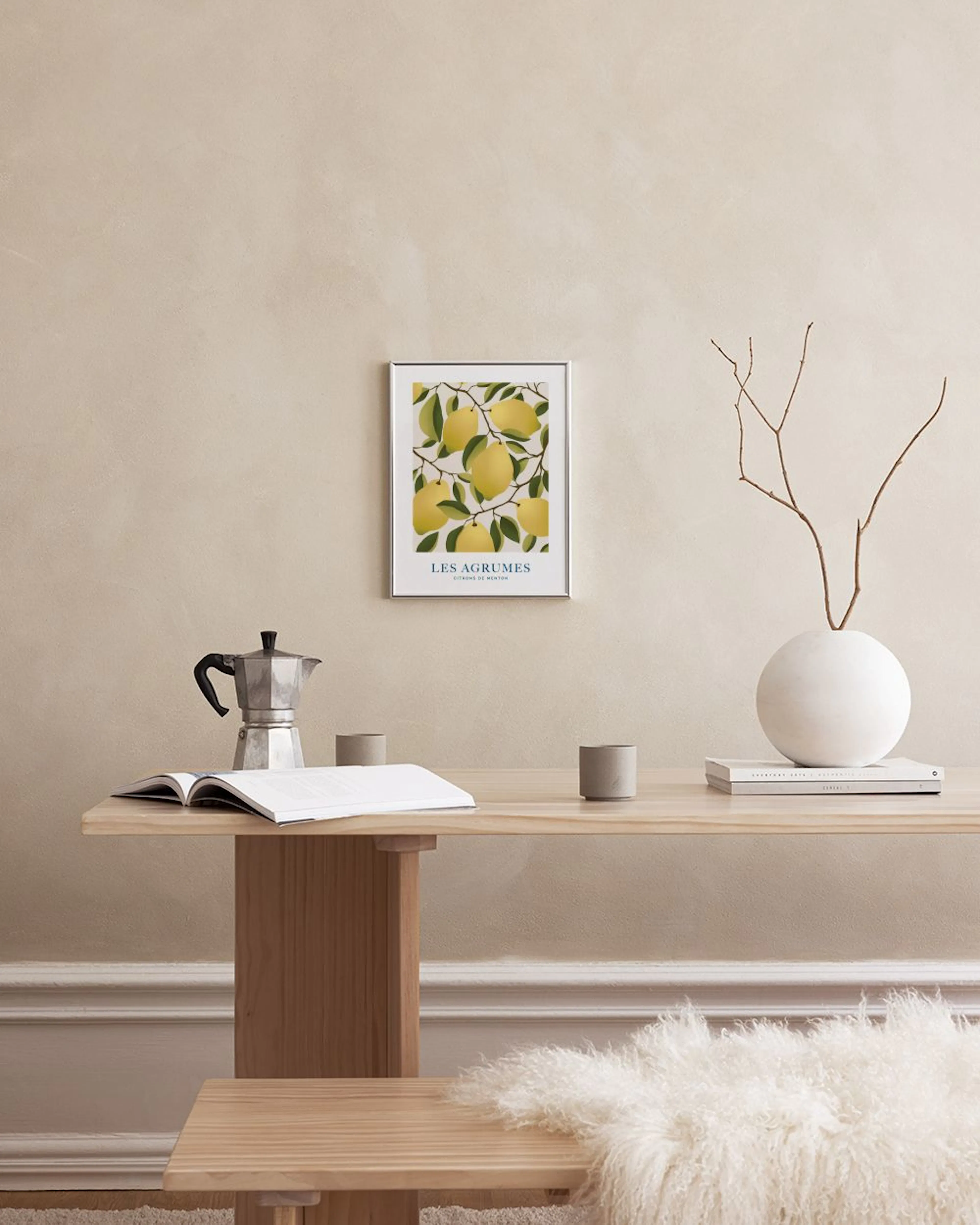 Póster de limones amarillos en ramas con hojas verdes, colgado sobre un mueble blanco con un jarrón y un libro abierto.