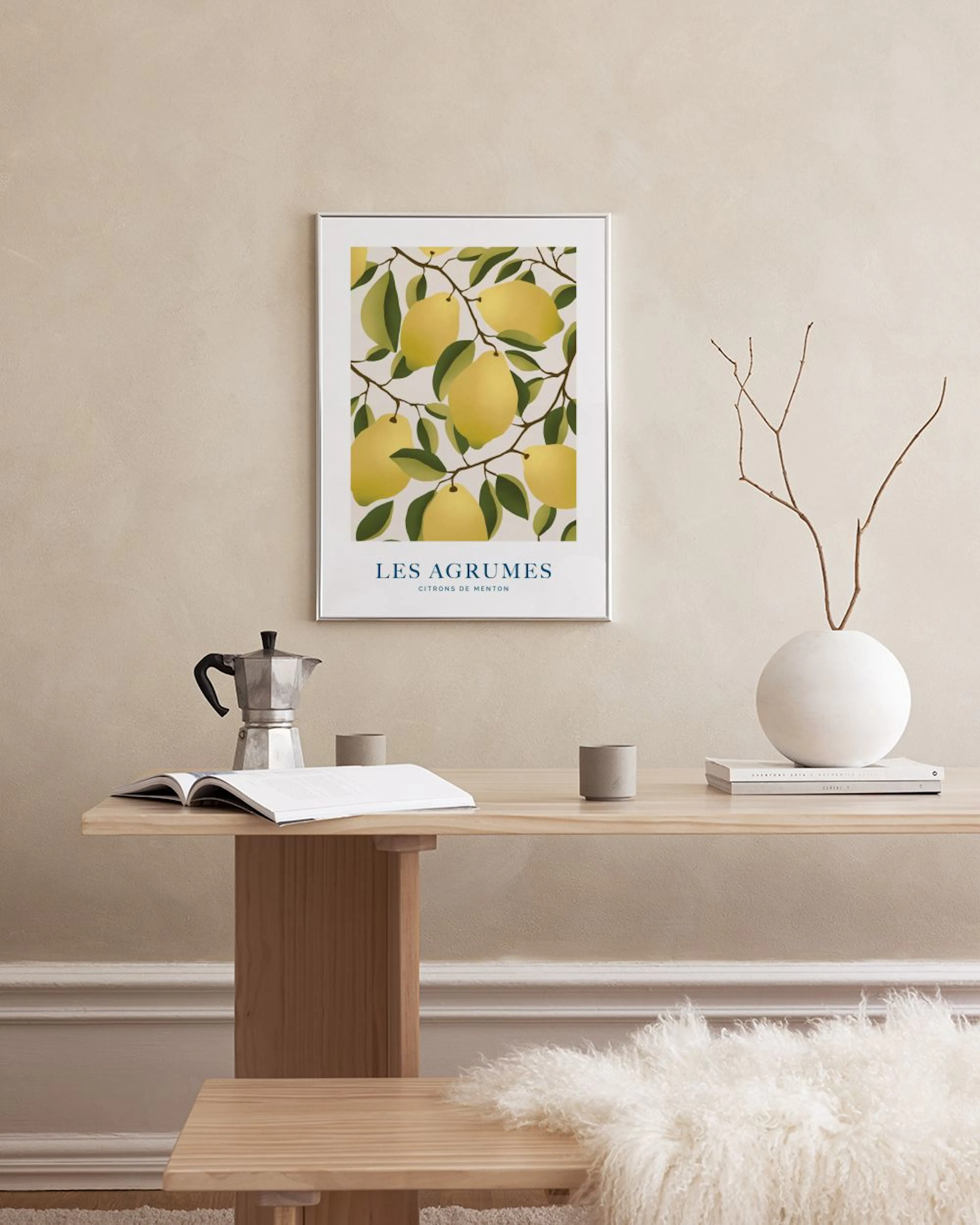 A lemon print with green leaves hanging above a white console table with a clear vase and open book.
