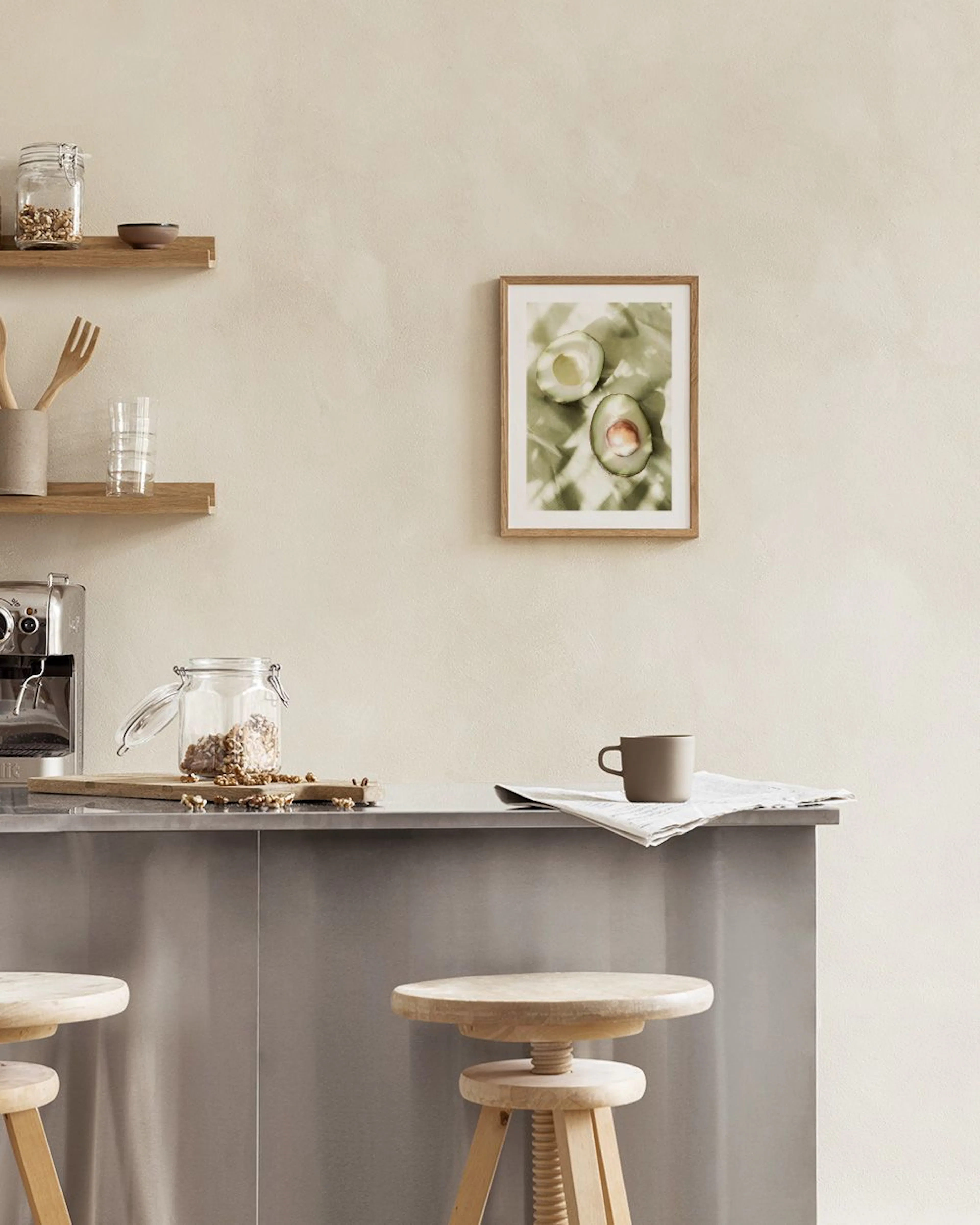 Póster de dos mitades de aguacate sobre tela verde con sombras, exhibido encima de un mueble blanco con tazas y botellas.