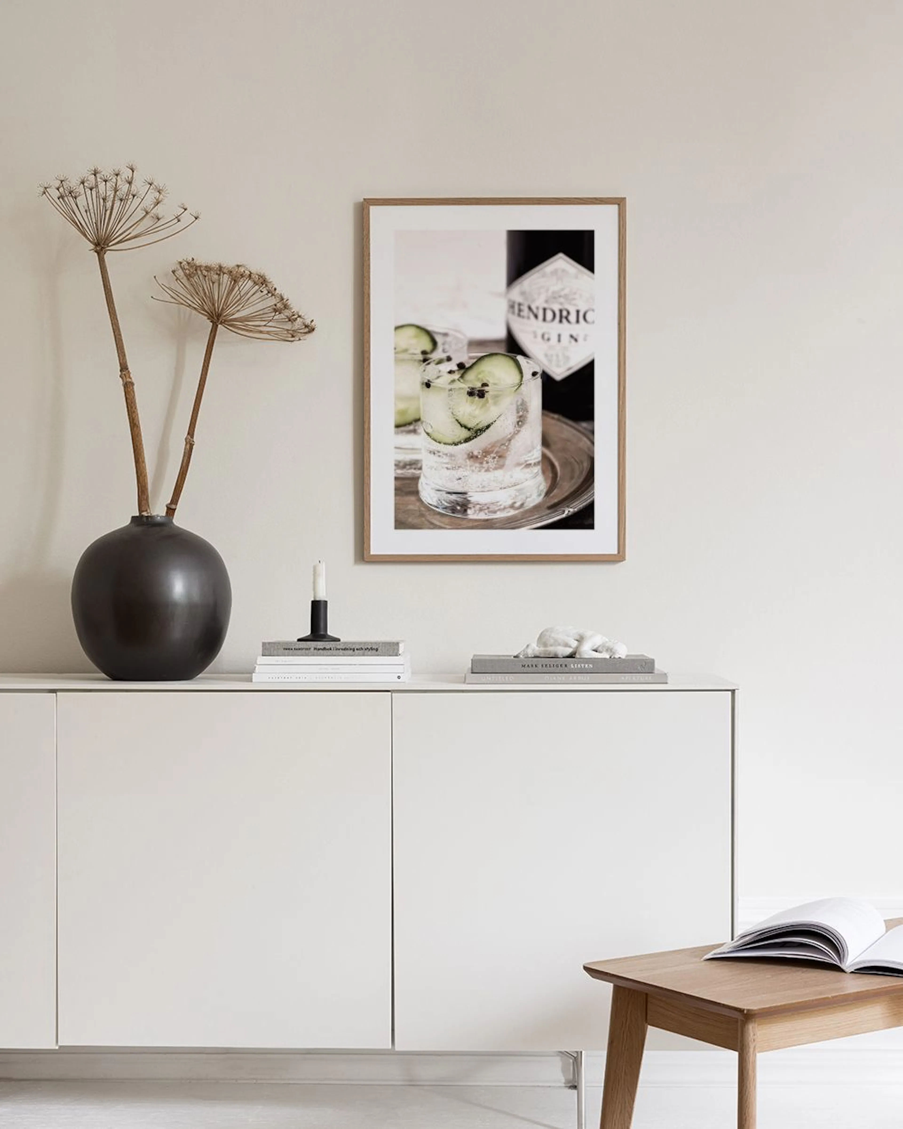 Poster mit Gin Tonic Gläsern, Gurkenscheiben und Pfefferkörnern, dazu eine Gin-Flasche, hängt über einem Regal mit Deko.