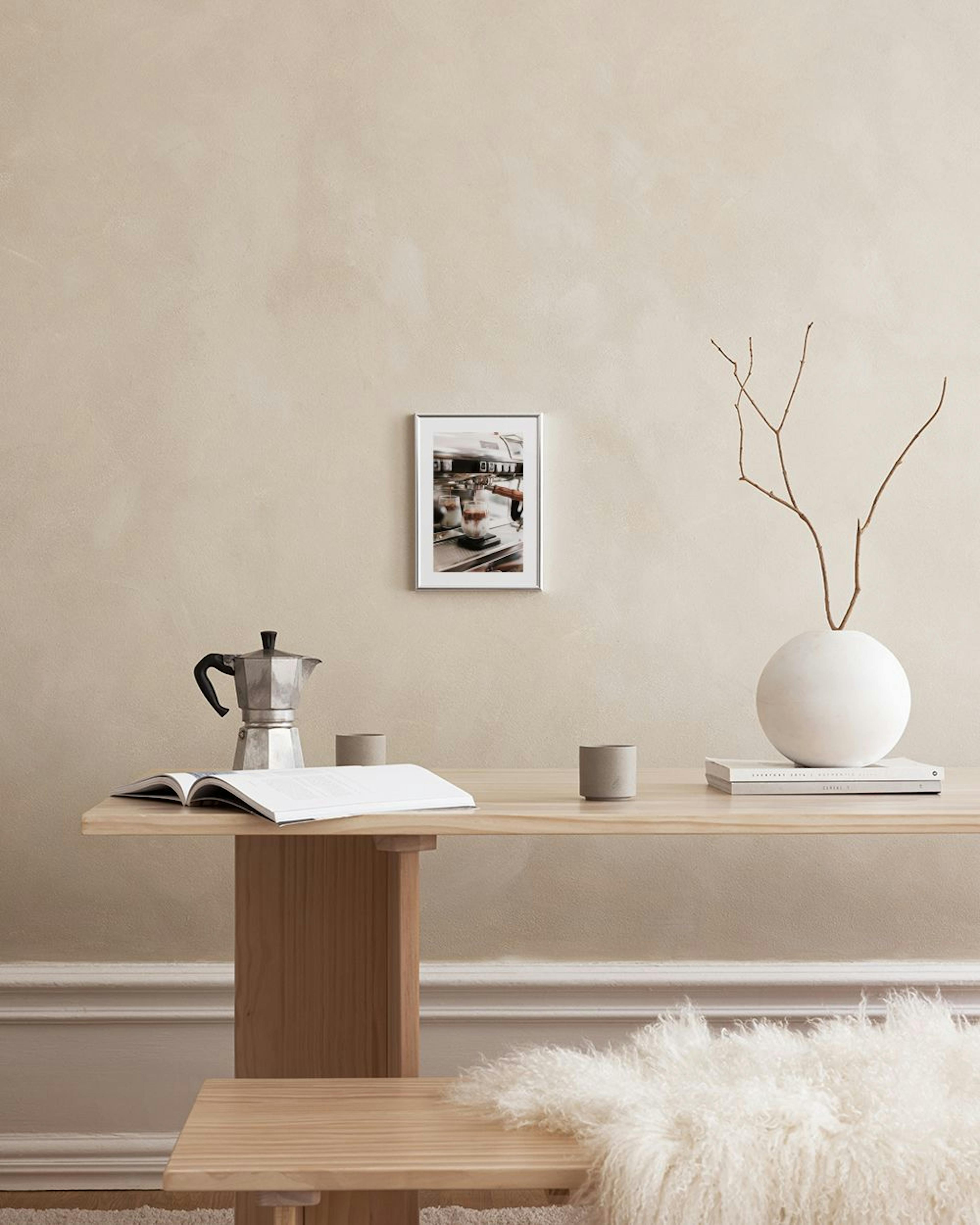 A print of espresso pouring into a glass of ice and milk, hanging above a white cabinet with coffee accessories.