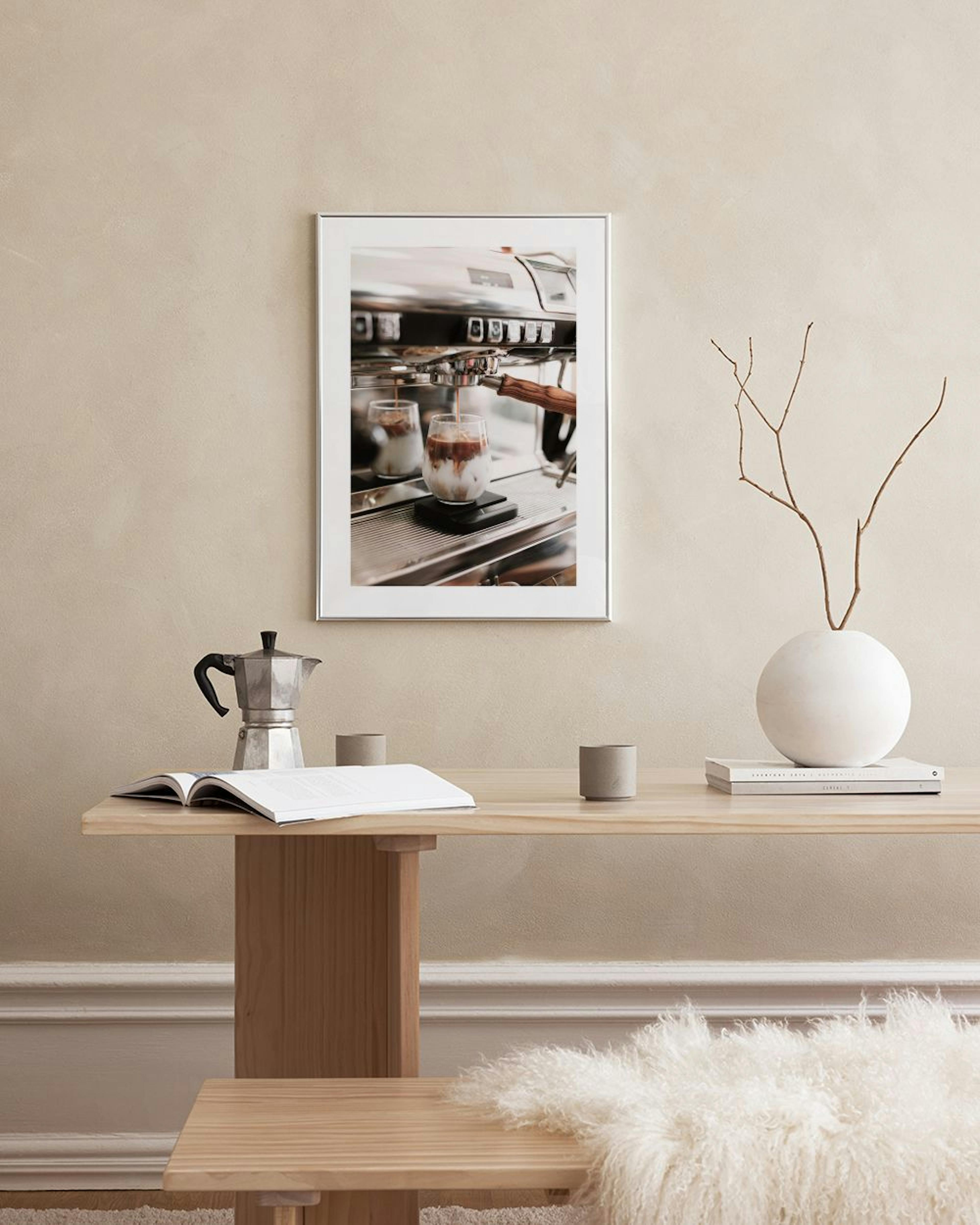 Póster de café helado vertiéndose en un vaso, junto a una máquina de café express, exhibido sobre un mueble blanco.