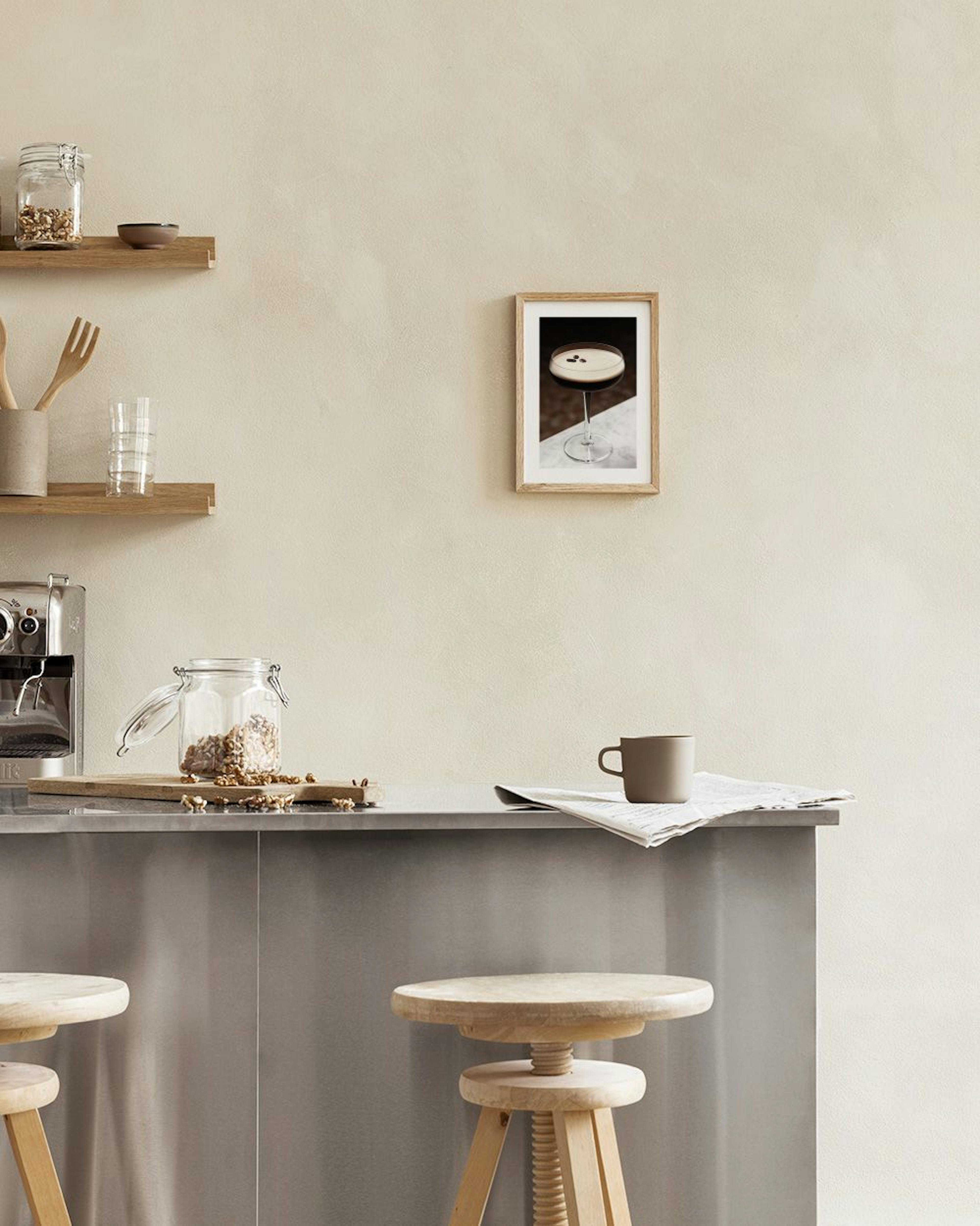 A print of an espresso martini with coffee beans floating on its foam, hanging above a white console table with a black vase and