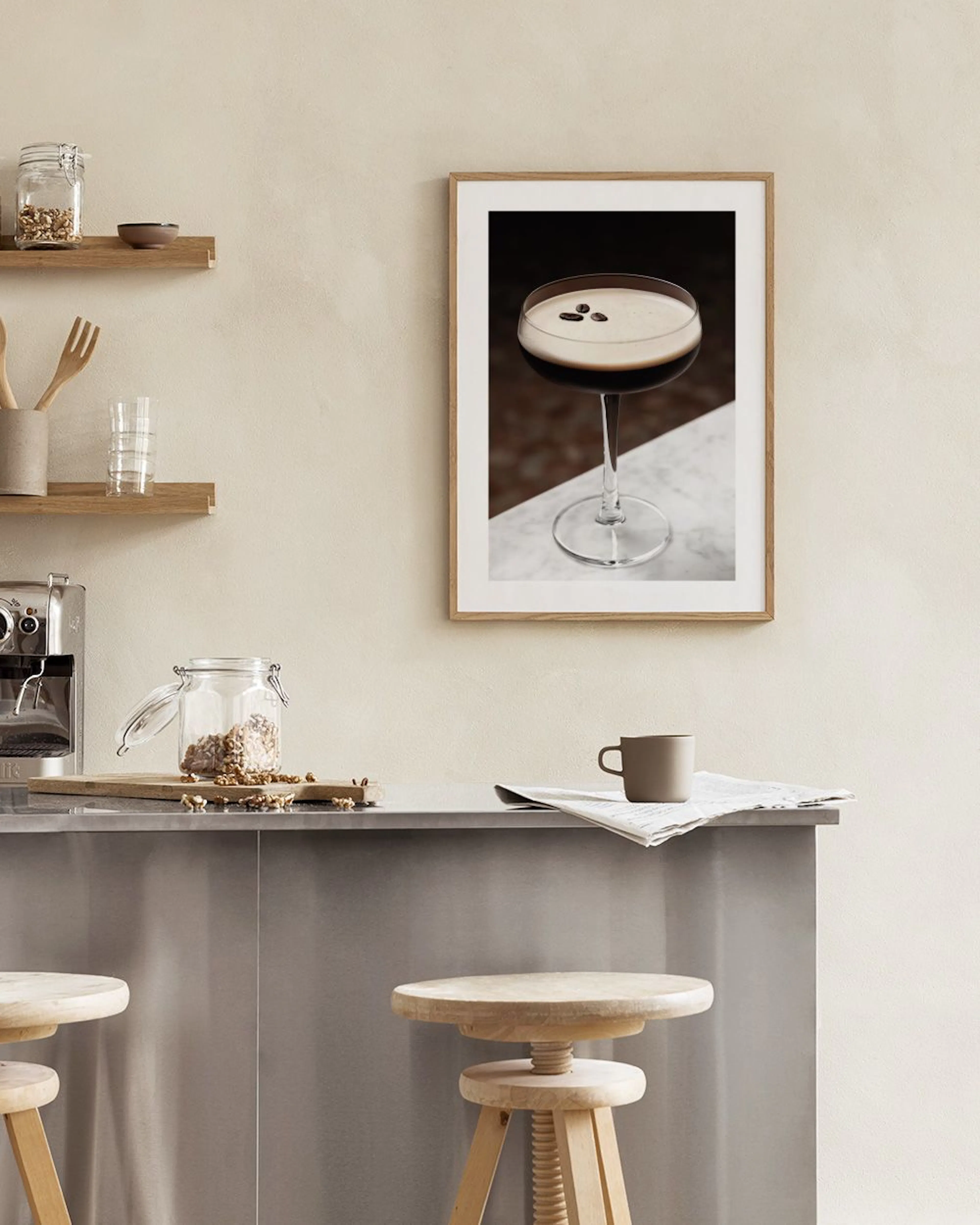 A print of an espresso martini with coffee beans floating on its foam, hanging above a white console table with a black vase and