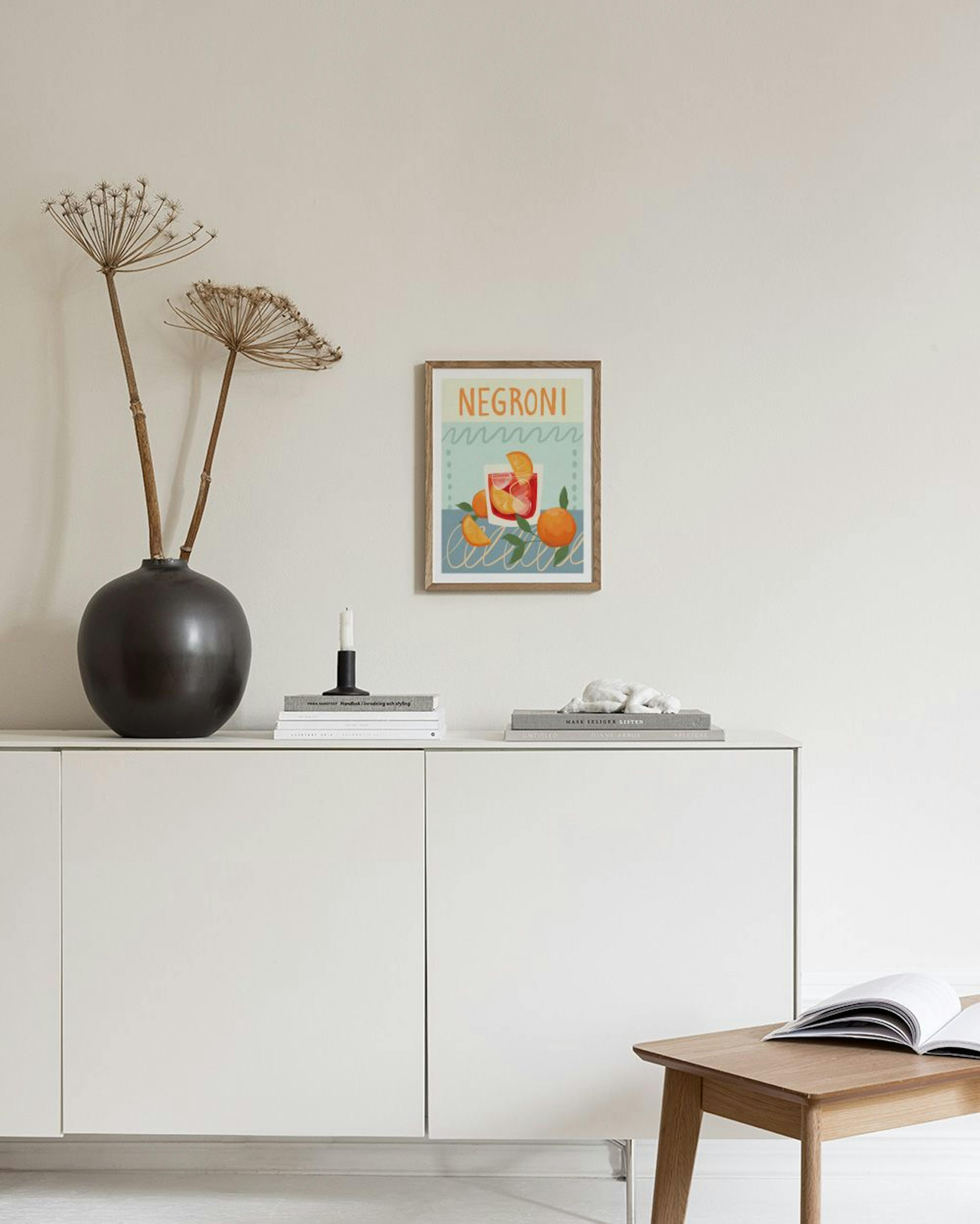 A Negroni cocktail print with oranges and leaves, displayed above a black console table in a living room.