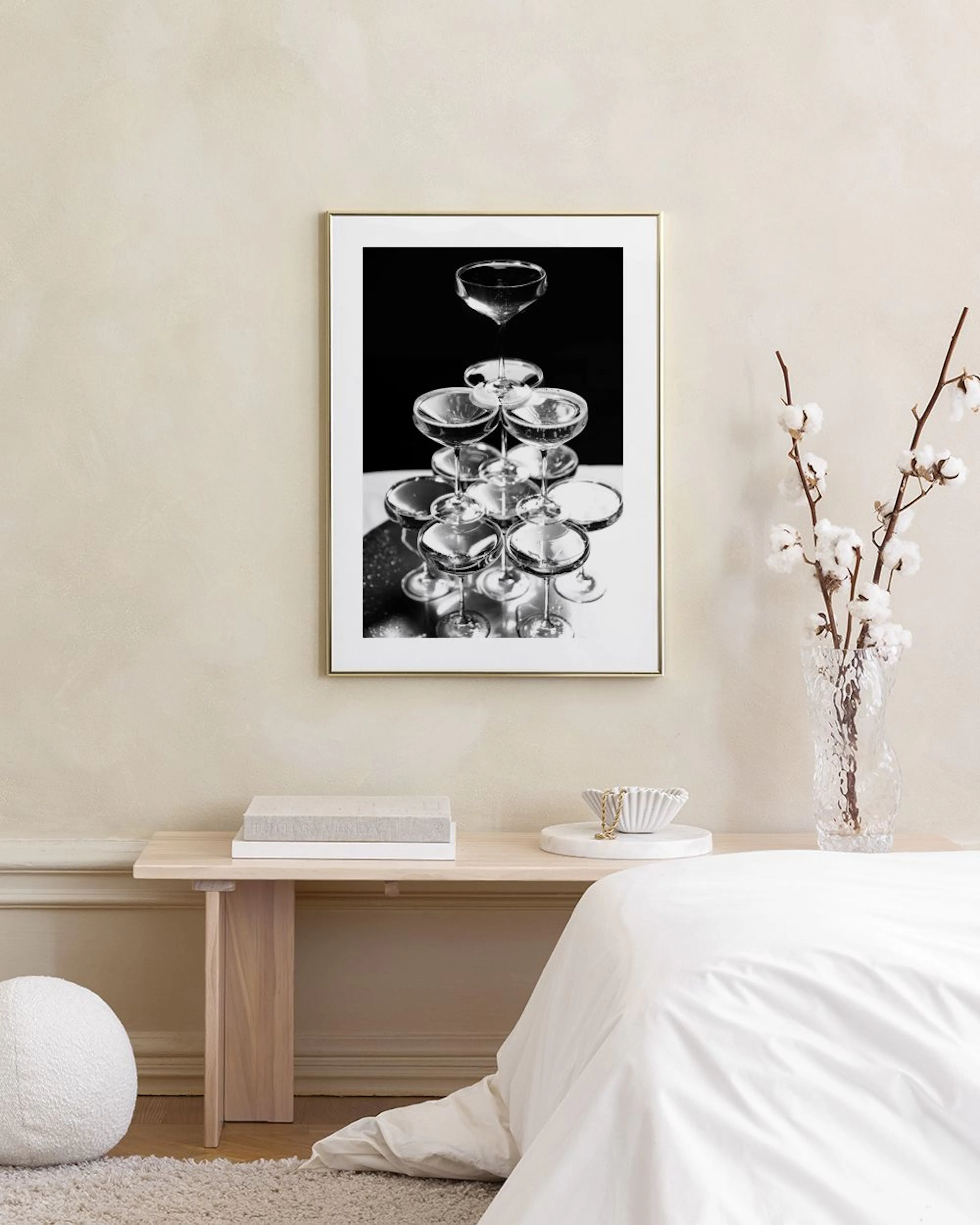 A black and white print of a champagne glass pyramid, hanging on a dark green wall above a matching green ottoman.