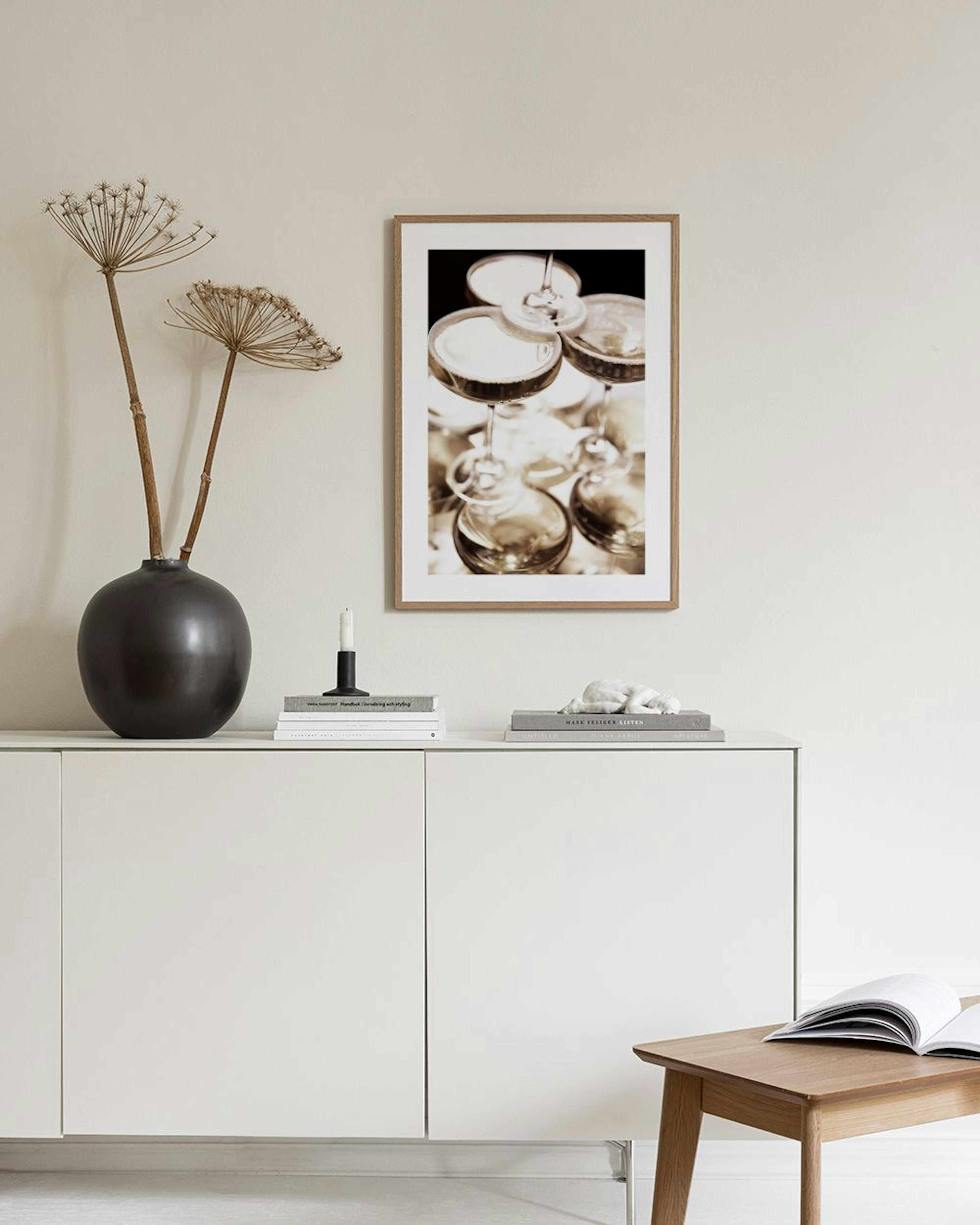 A print of stacked champagne coupe glasses with bubbly liquid, displayed on a dark blue wall with a blue velvet ottoman below.
