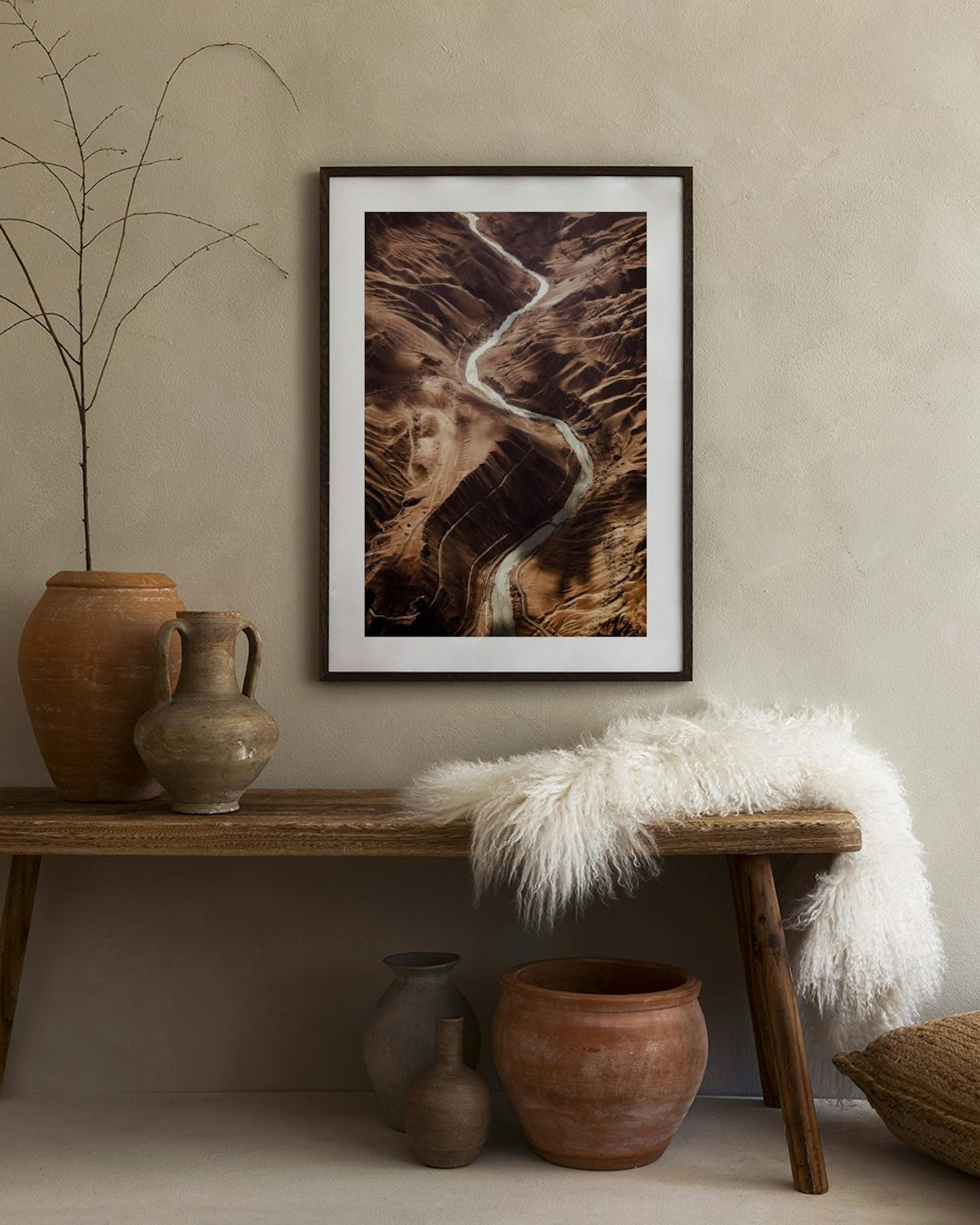 Poster mit Luftbild eines sich schlängelnden Flusses durch eine braune Wüstenlandschaft, hängend über einem weißen Sideboard mit