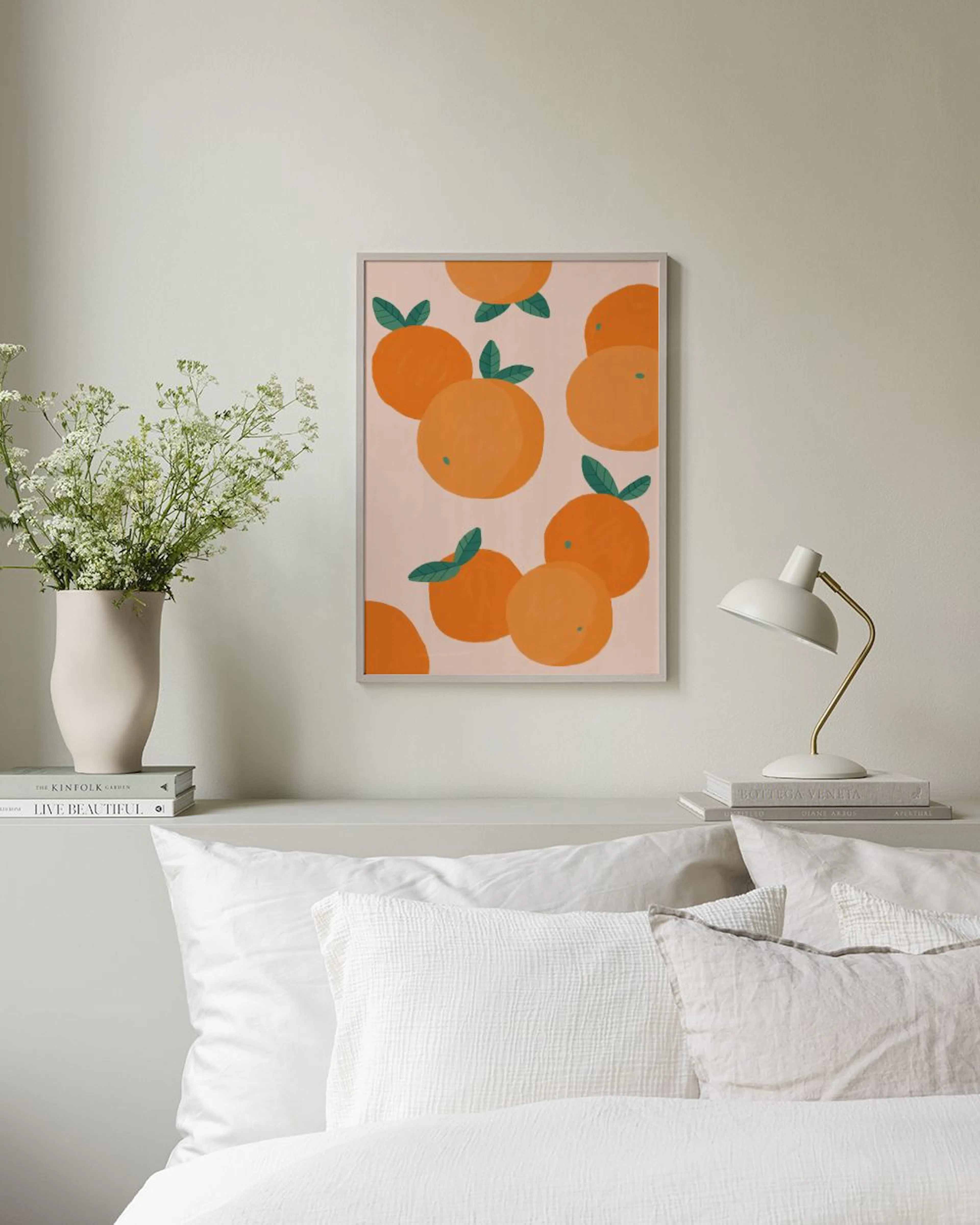 Plakat med illustrasjon av oransje appelsiner med grønne blader, henger på en rosa vegg over en hvit kommode.