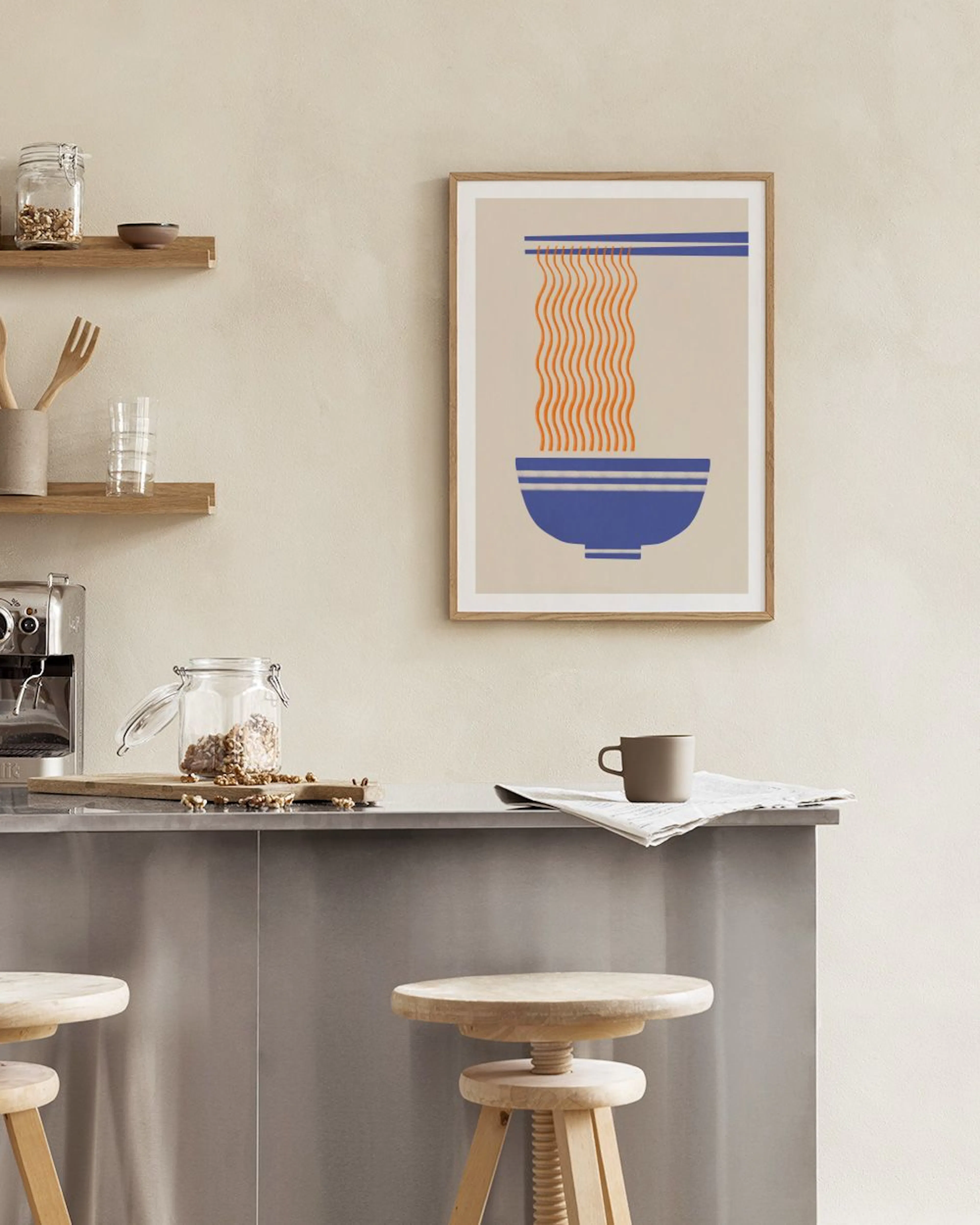 Poster met abstracte oranje noedels in een blauwe kom, hangend aan een witte muur boven een eettafel.