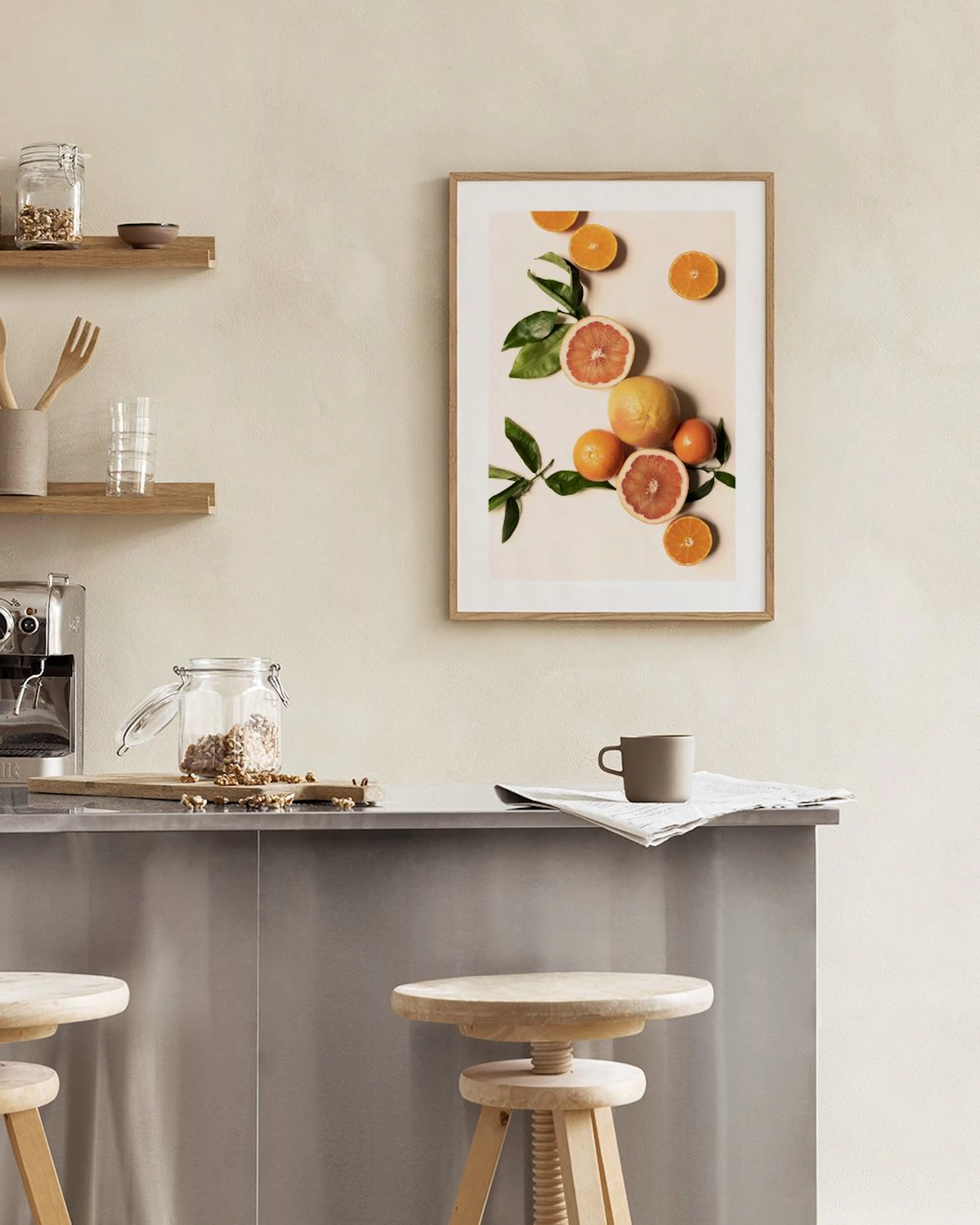 A print of grapefruits and oranges with green leaves, displayed on a white wall in a dining room with a book and wooden chair.