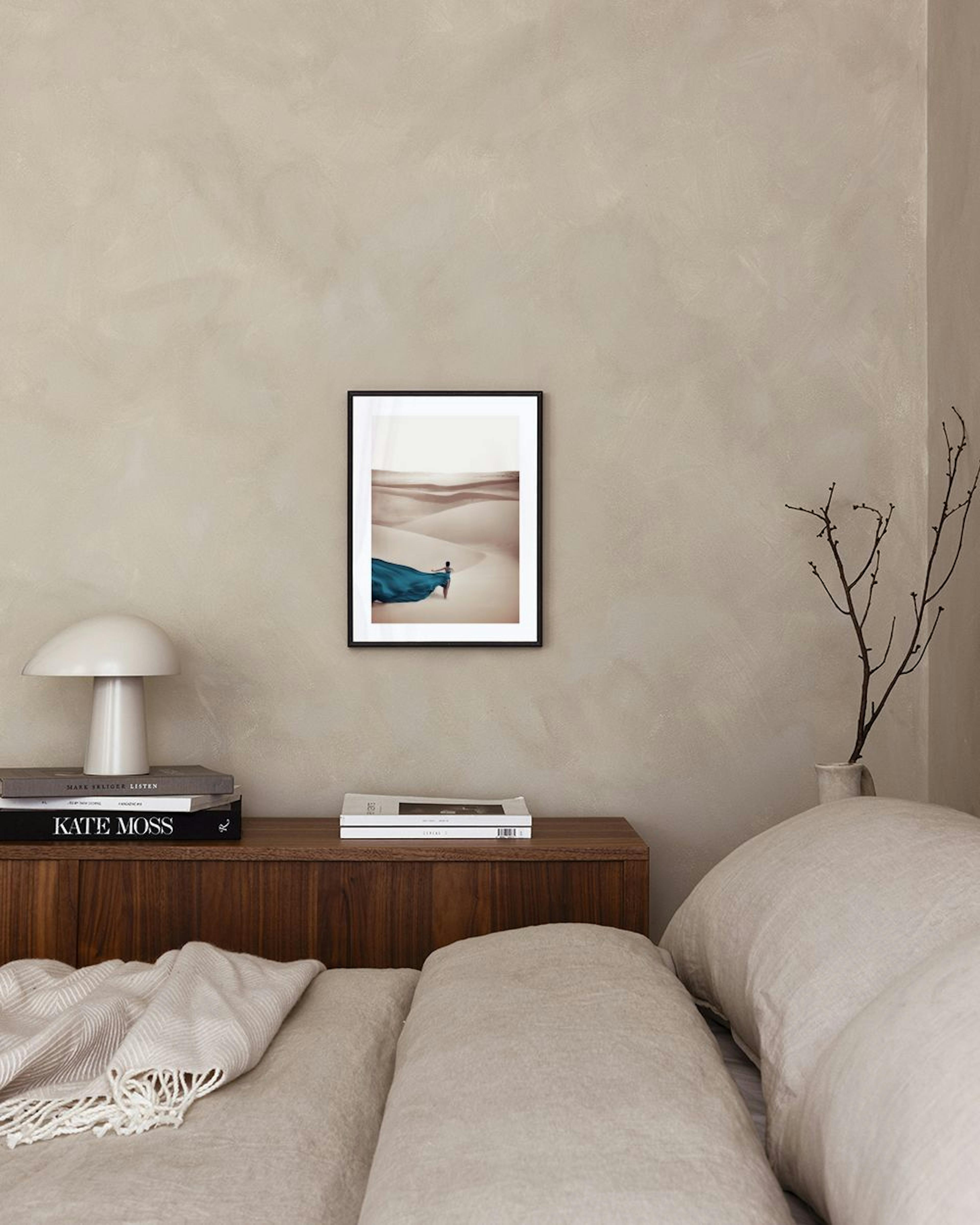 A print of a woman in a flowing blue dress walking on sand dunes, displayed above a modern brown and black cabinet with decorati