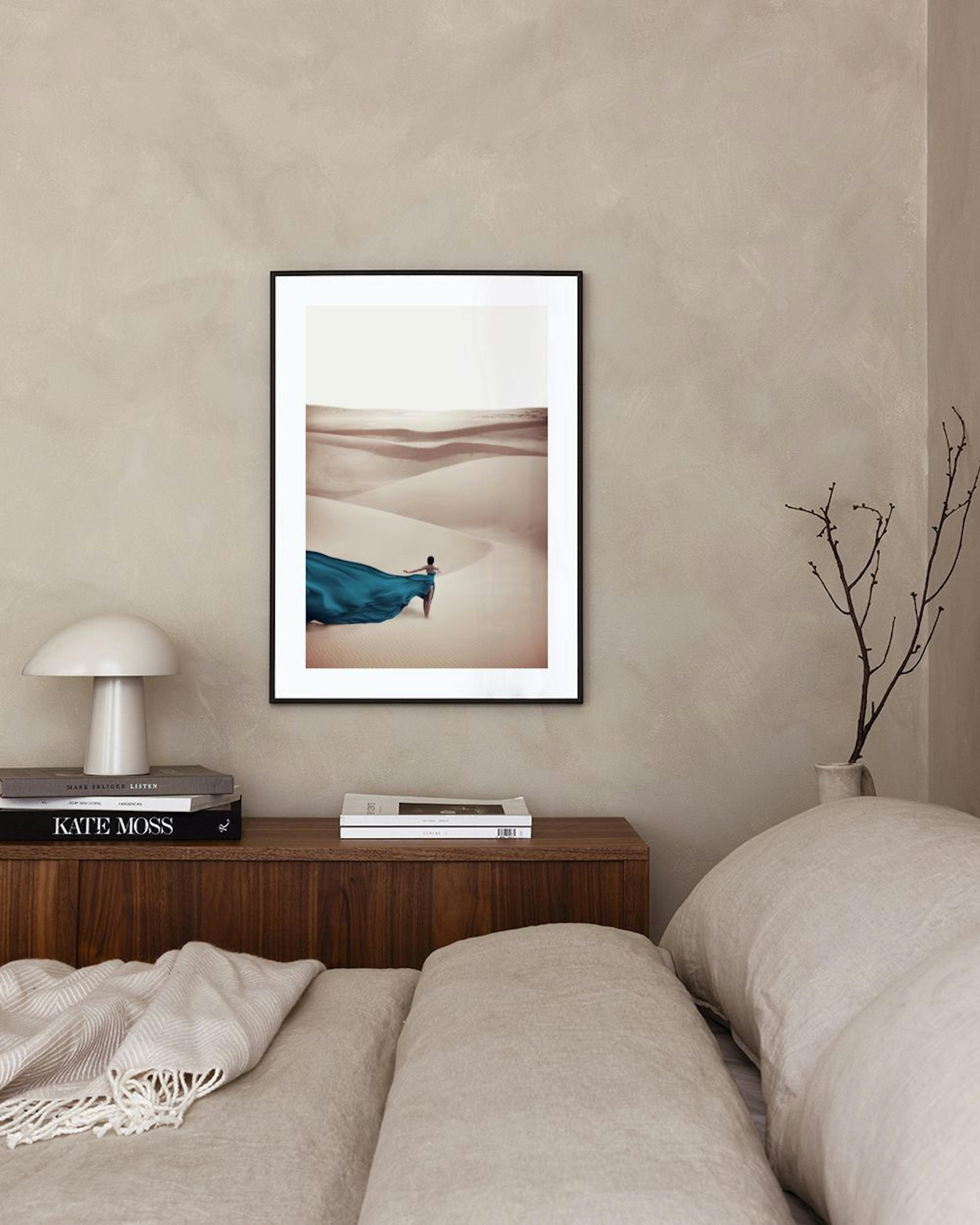 A desert print with a person in a flowing blue dress walking across sand dunes, displayed above a beige cabinet with decorative 