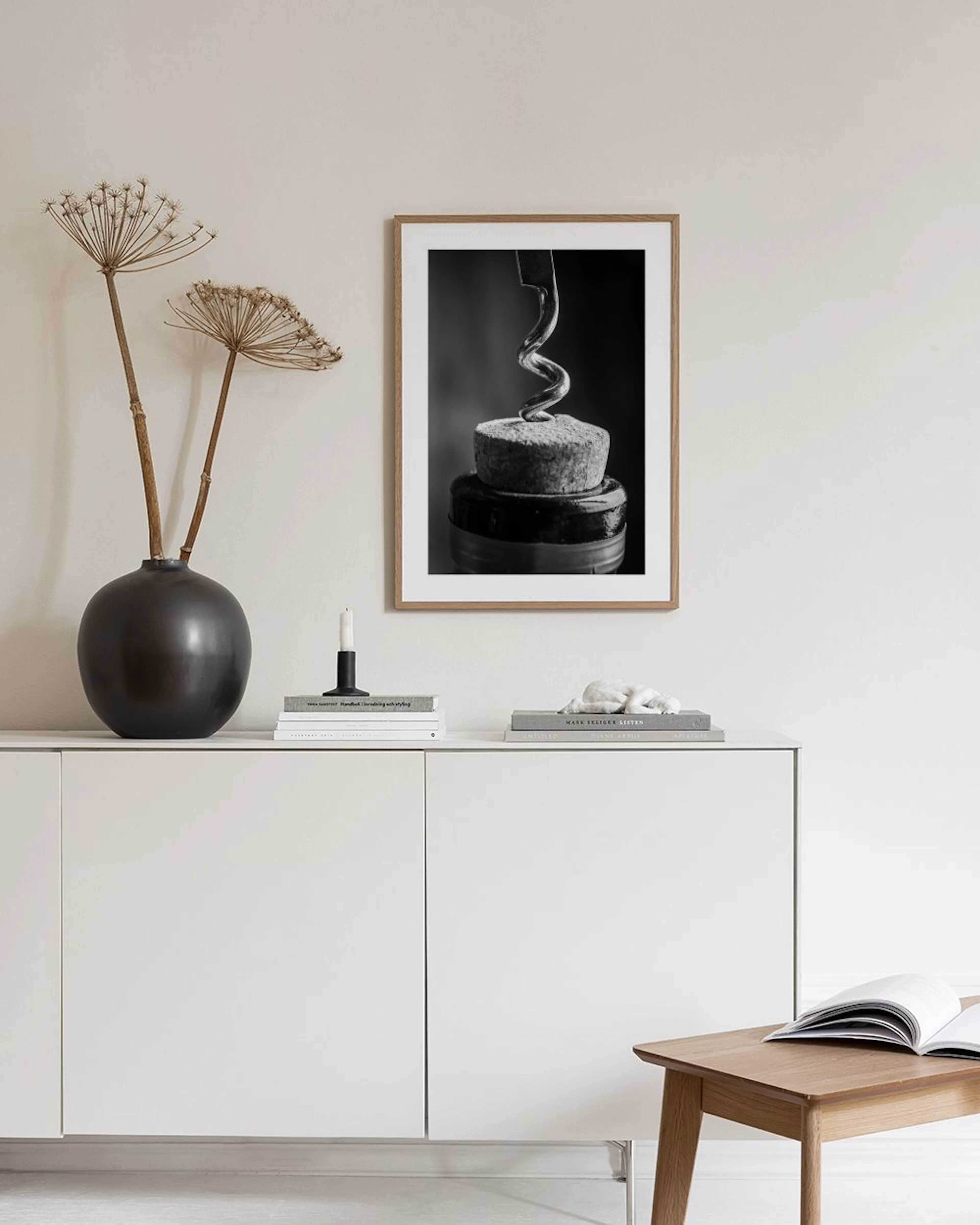 A black and white print of a corkscrew entering a cork, displayed in a modern dining room above a white table with an open book.