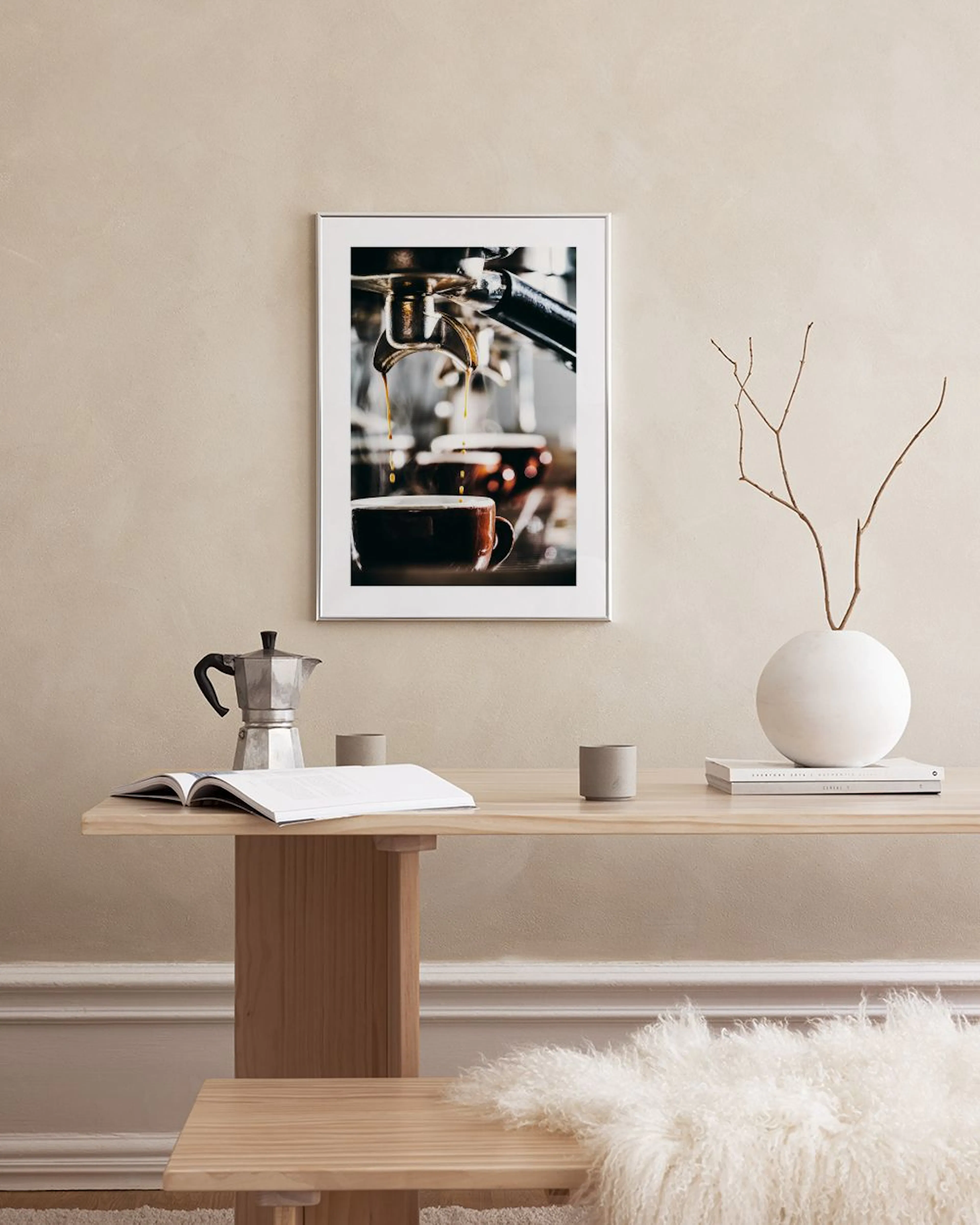 Poster van een espressomachine die koffie in een kopje schenkt, hangend boven een tafel met een boek en een stoel.