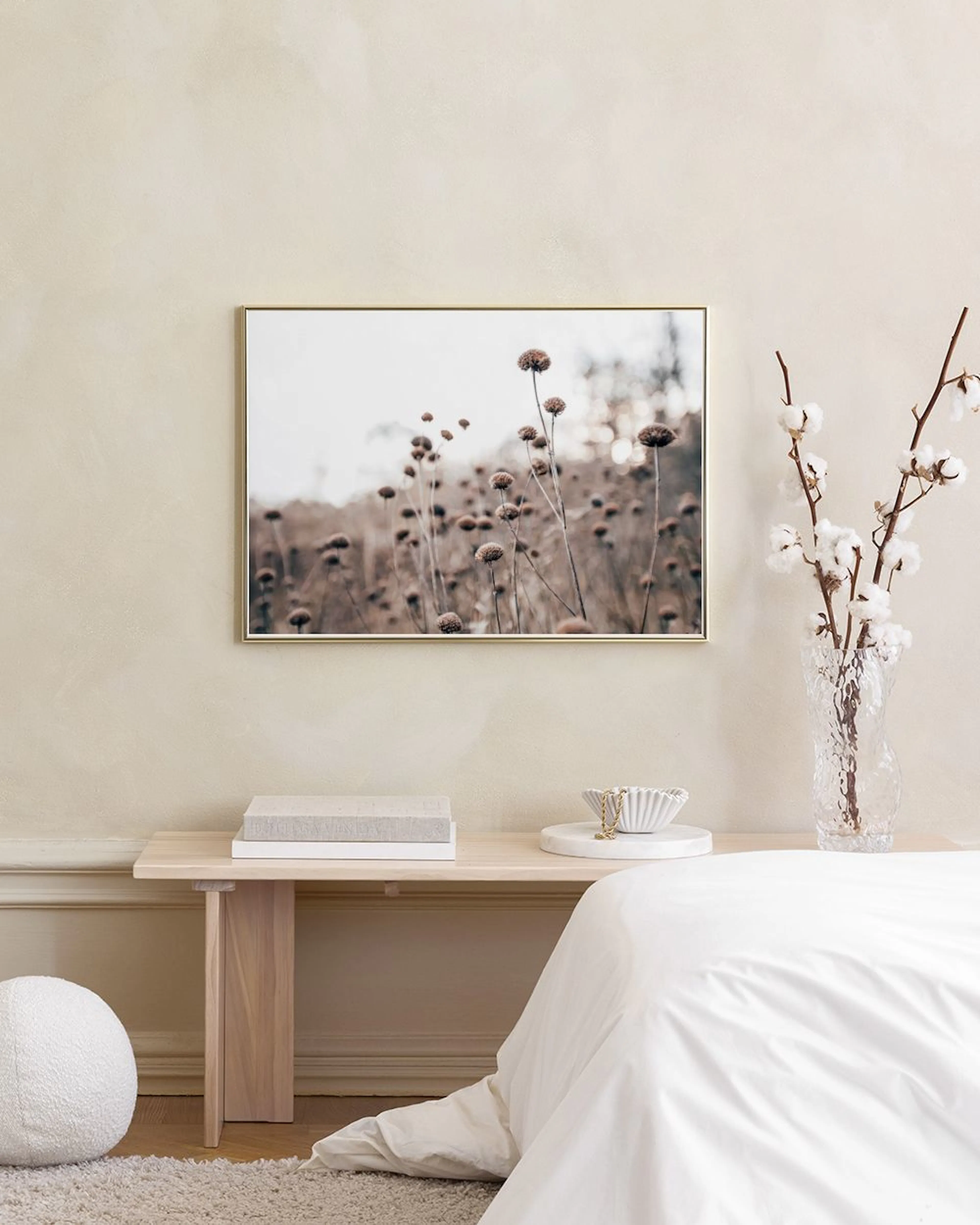 Plakat med tørre blomster i brunt og beige, henger på en lys grå vegg over to gullfargede bord.