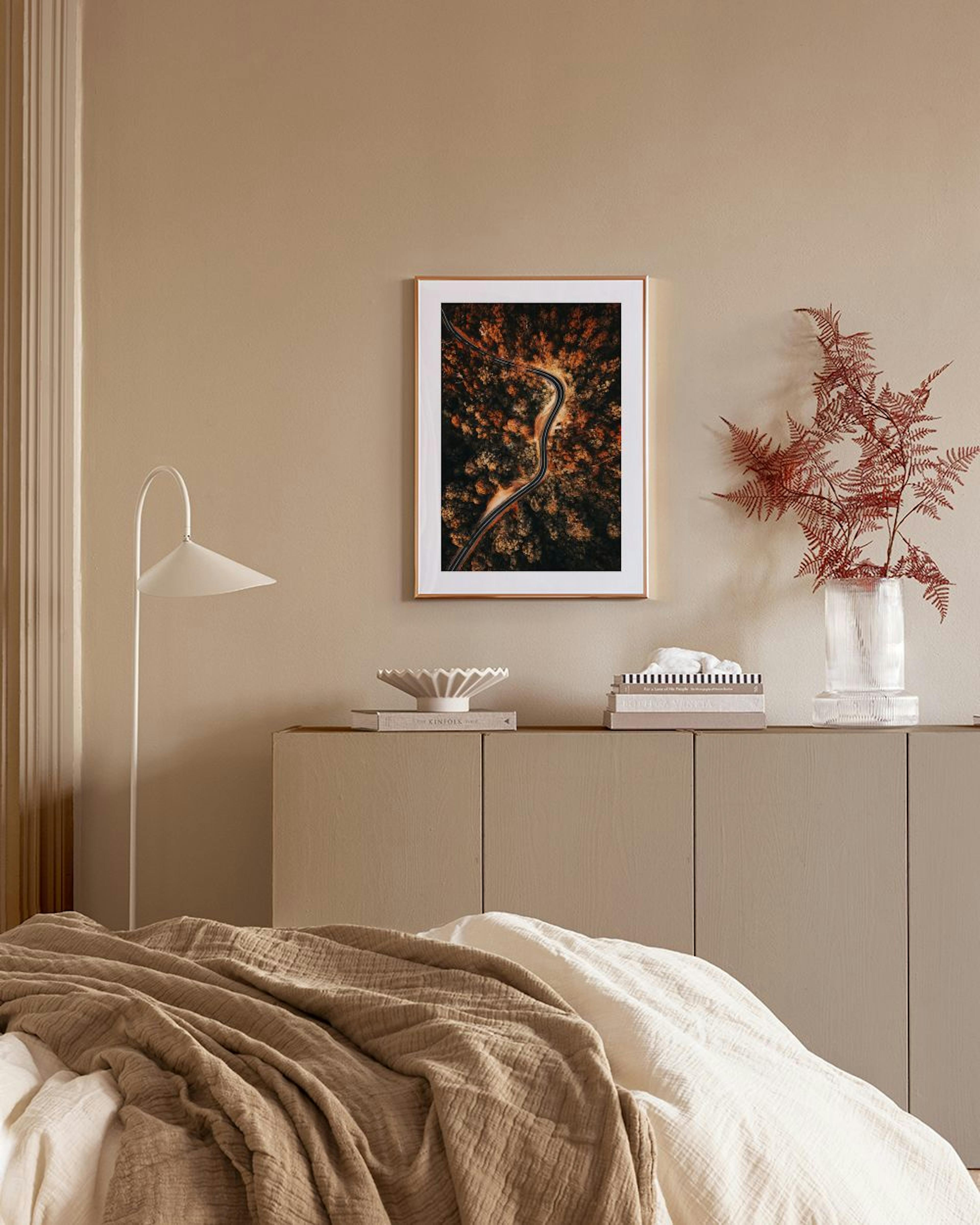 Poster mit Luftbild einer kurvigen Straße durch einen Herbstwald, über einem Sideboard mit Lampe.