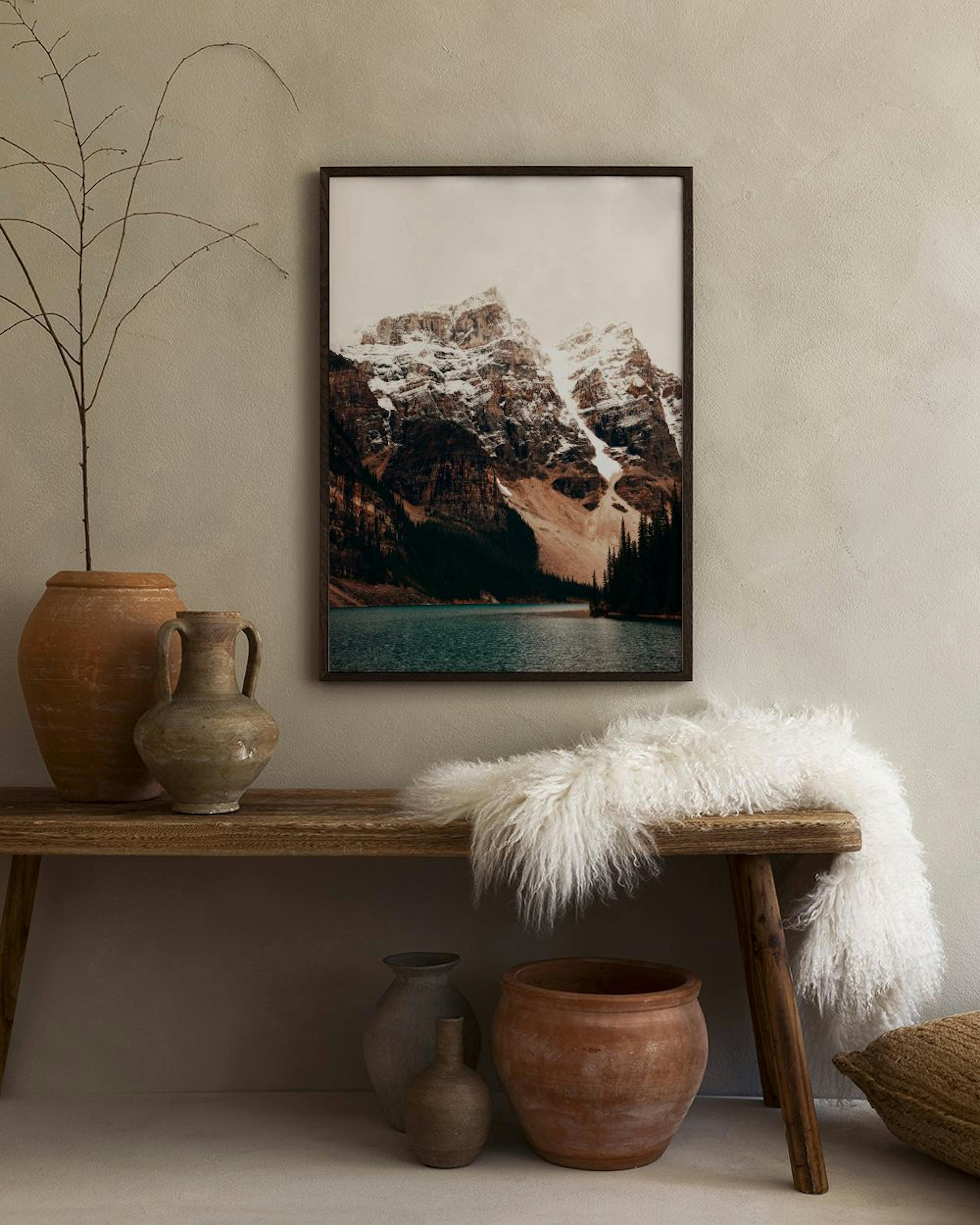 A stunning mountain landscape print with a turquoise lake, hanging above a cork stool with books on a white wall.