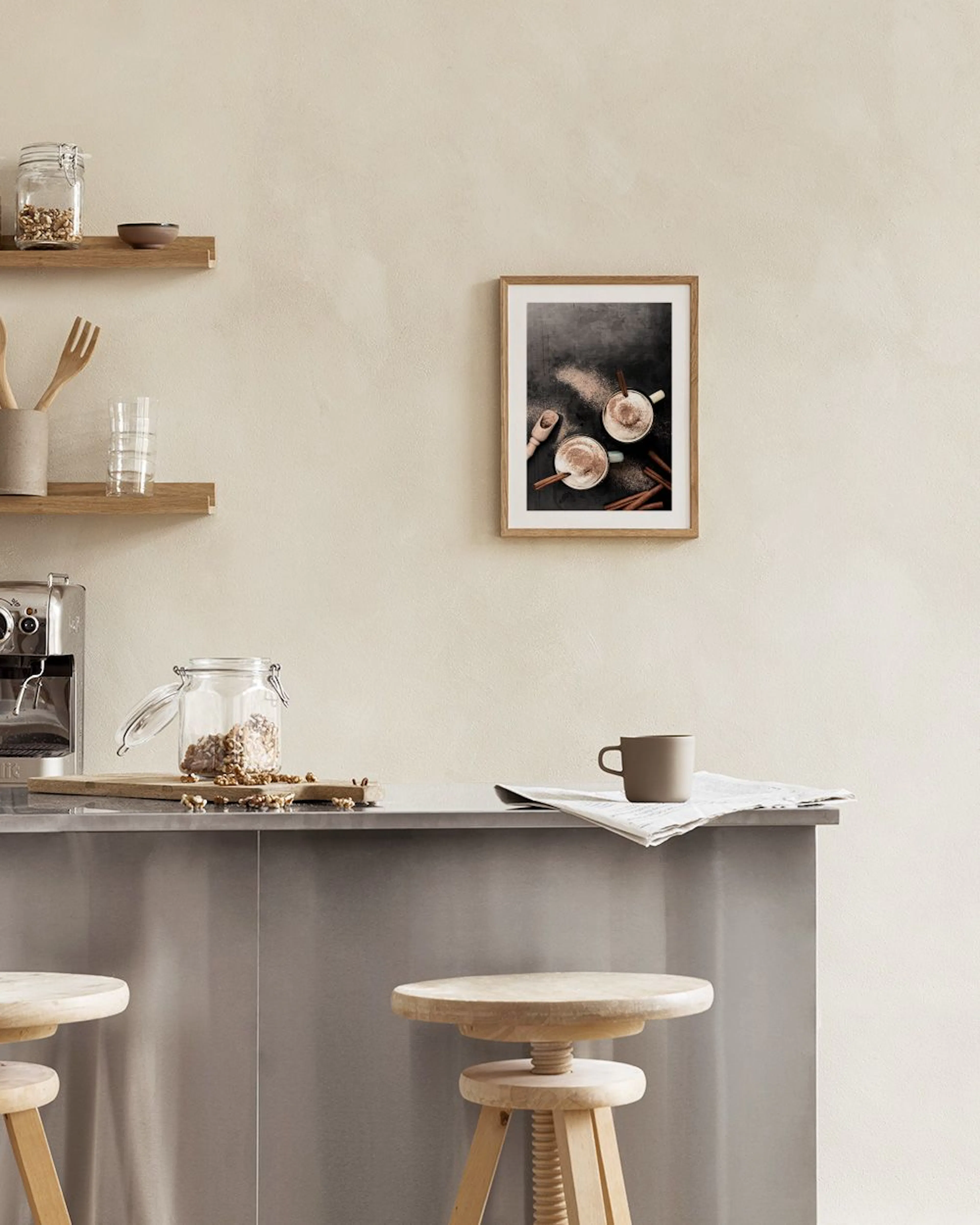 A print of two mugs of hot cocoa with cinnamon and a wooden scoop on a dark background, hanging in a modern dining room.