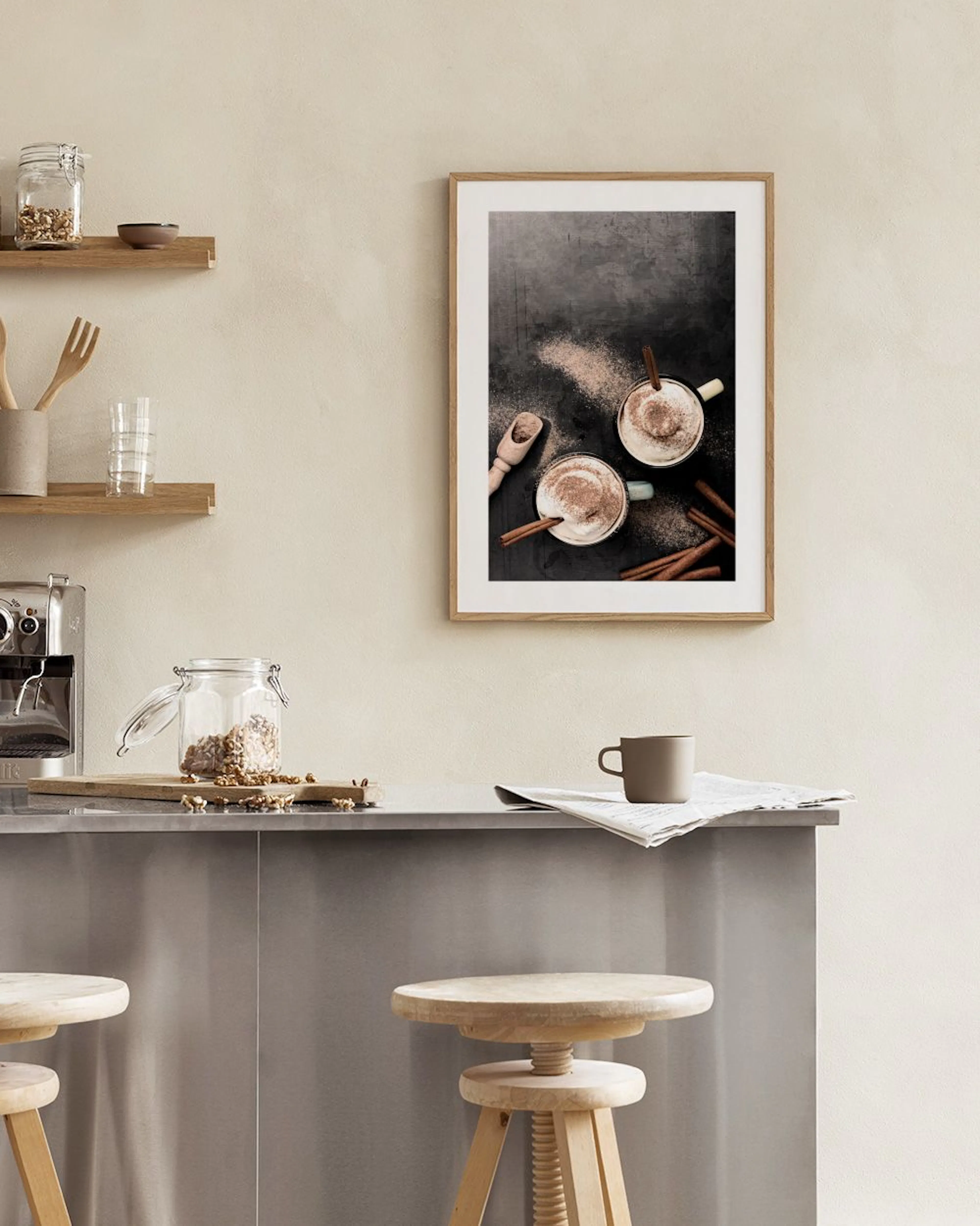 Poster mit zwei Tassen Kakao und Zimtstangen, hängt über einem weißen Tisch mit Buch und Stuhl.