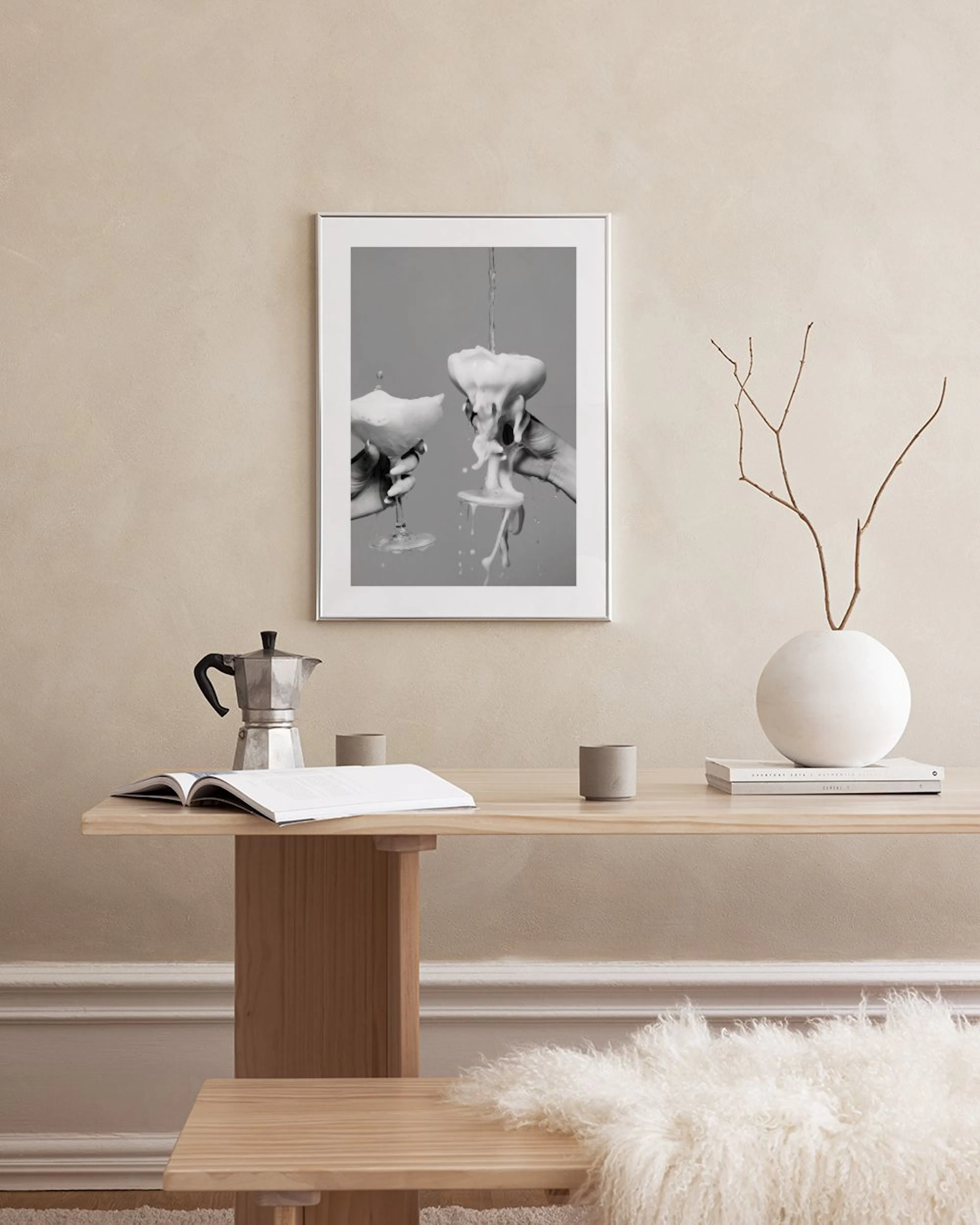 En plakat med to hænder, der holder champagneglas fyldt med skum, hængende over et hvidt skab med en grå vase.