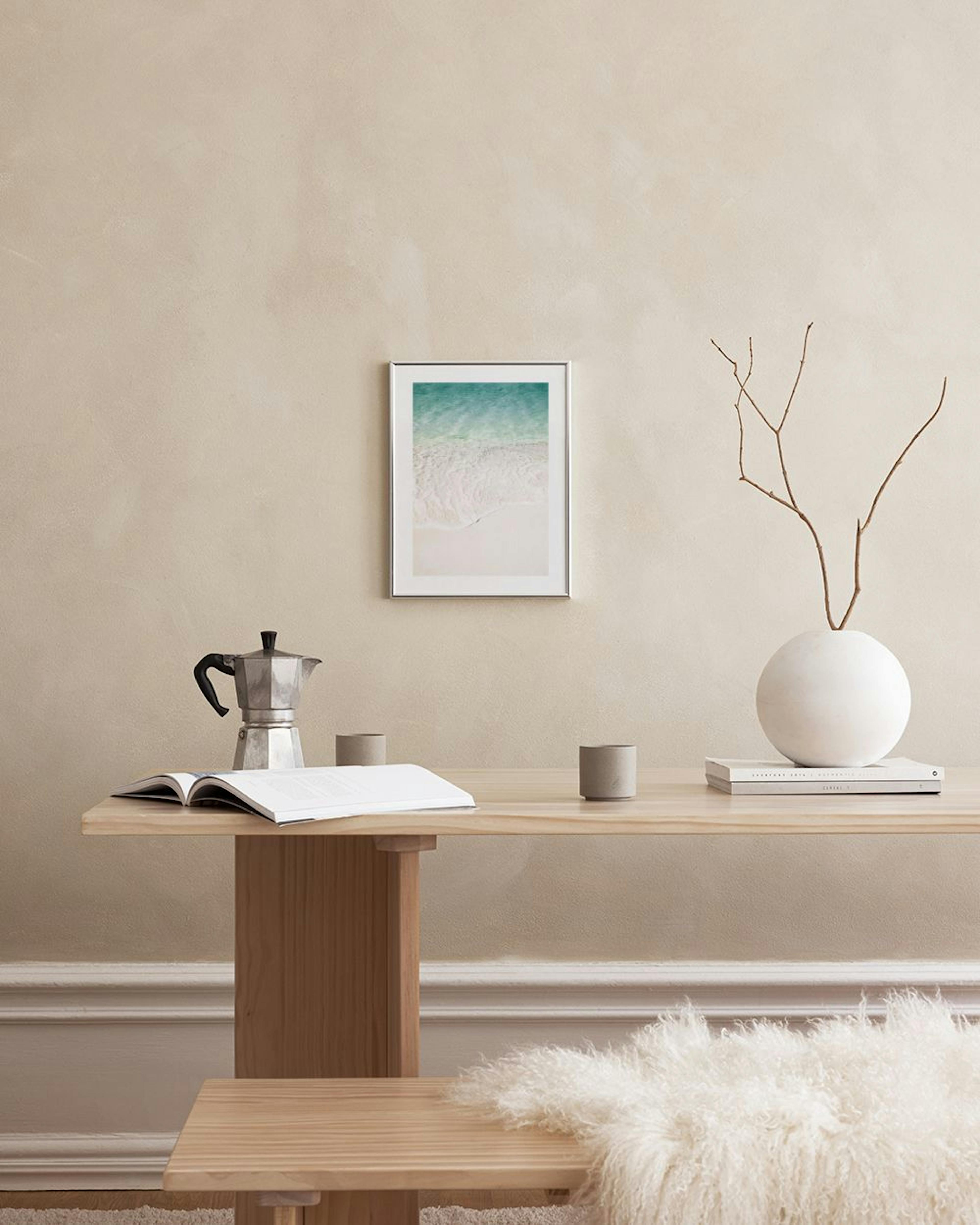 Poster van wit zandstrand met turquoise zeewater, hangend in een slaapkamer boven een betonnen nachtkastje.
