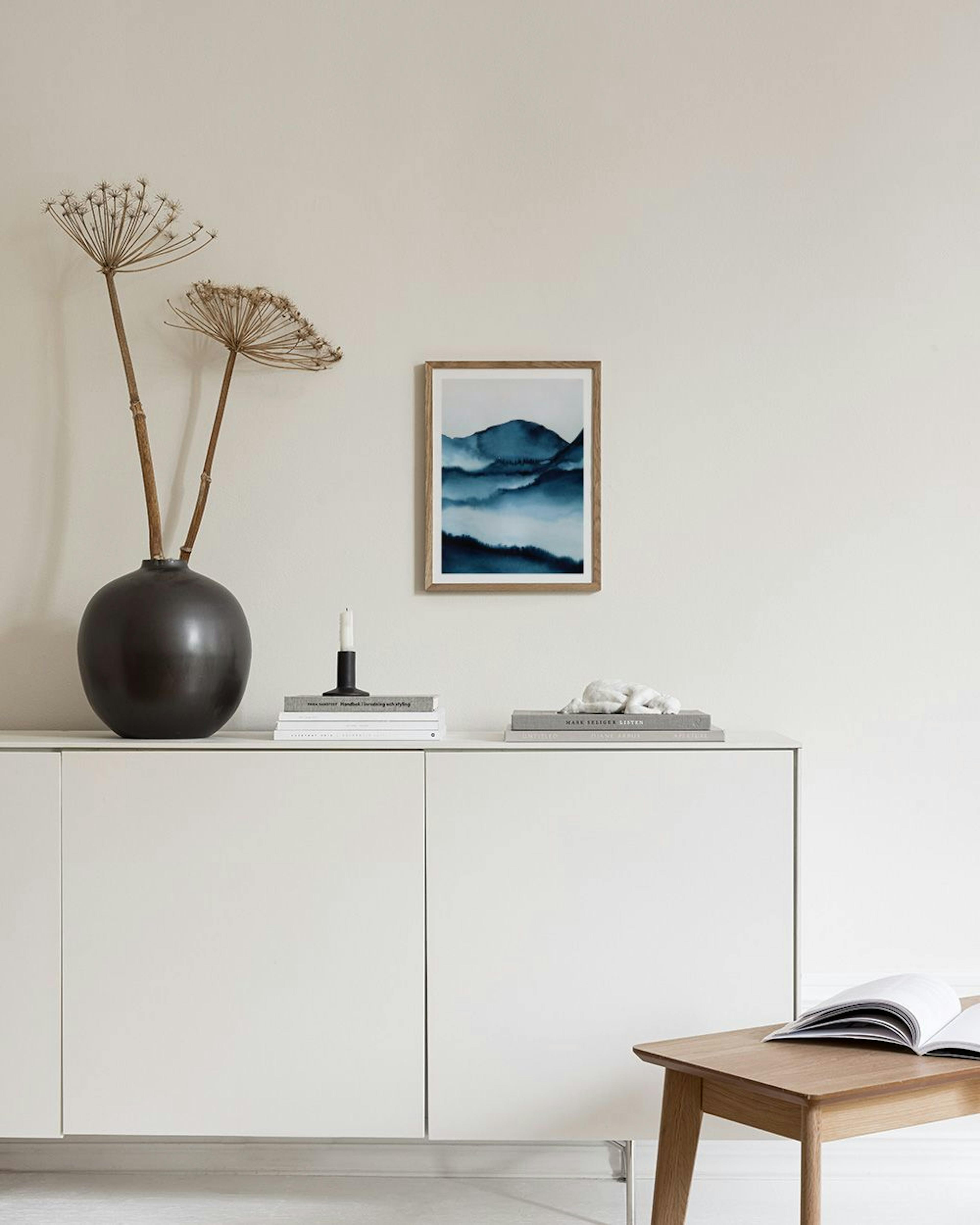 Poster mit blauen Bergen in Aquarell-Optik, hängt über einem Sideboard mit blauen Vasen.