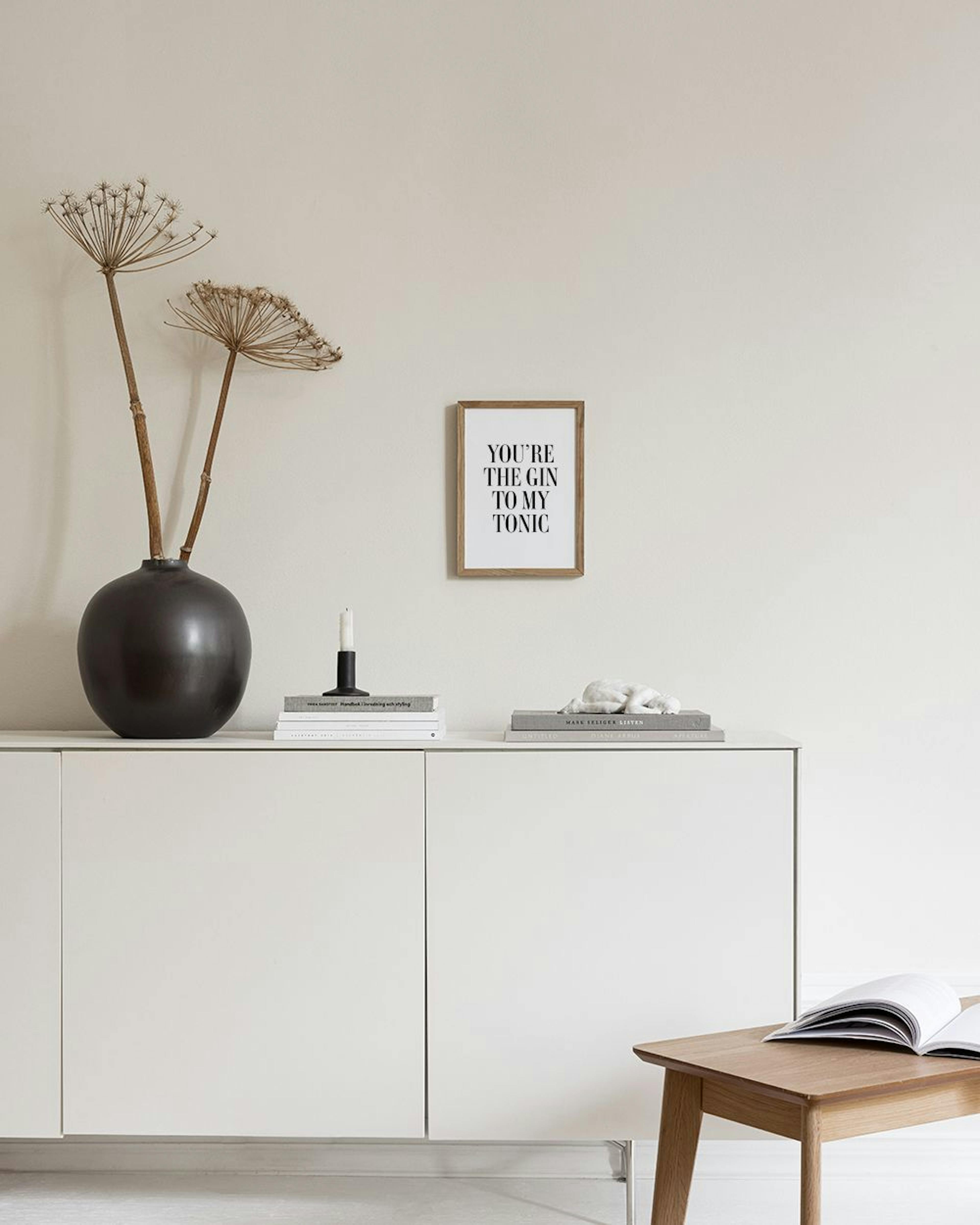 Ein Poster mit dem Spruch YOURE THE GIN TO MY TONIC an einer weißen Wand, über einem weißen Sideboard mit Vase.
