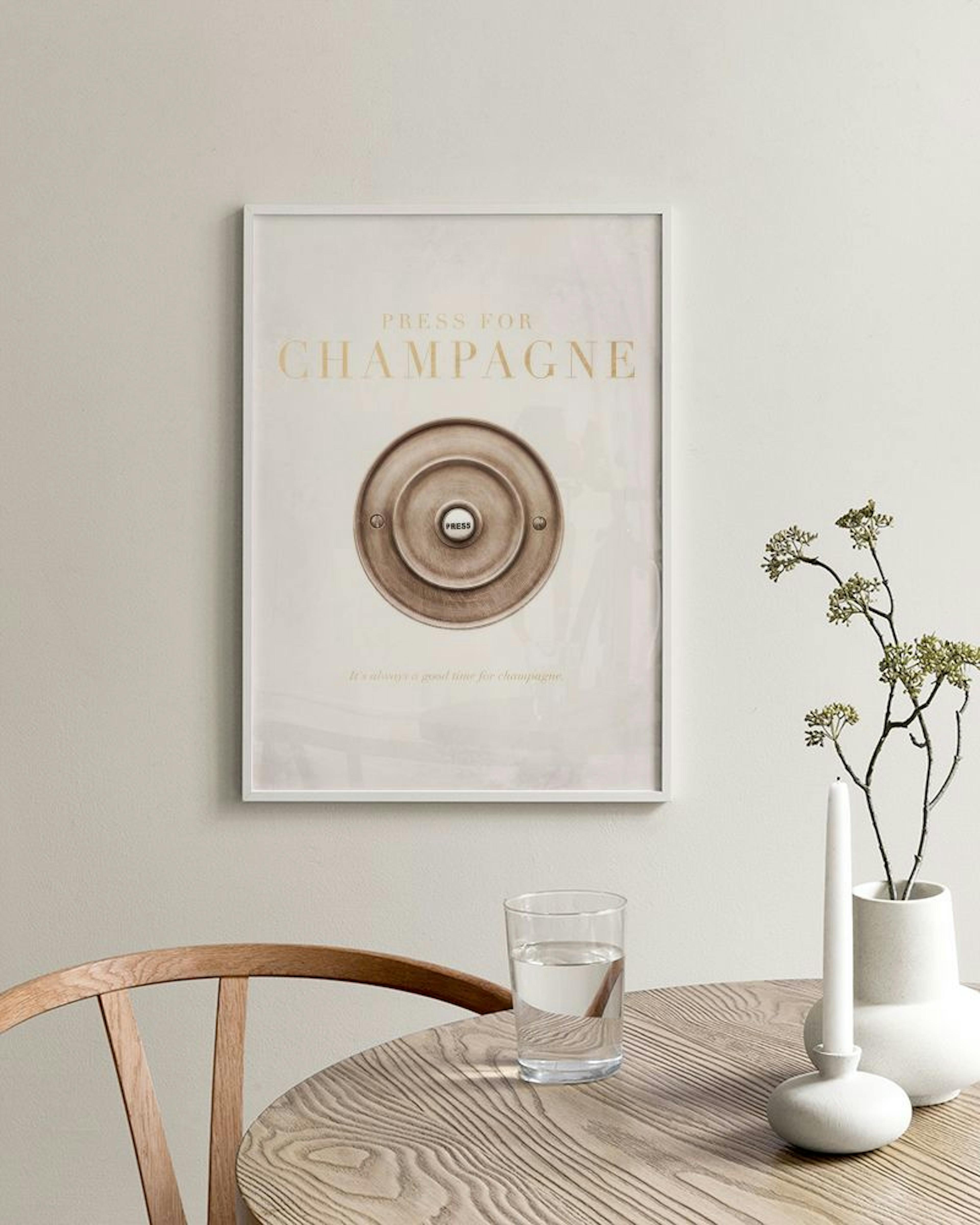 A print with the text Press for Champagne and a vintage bell button, displayed on a white console table with a vase and plant.
