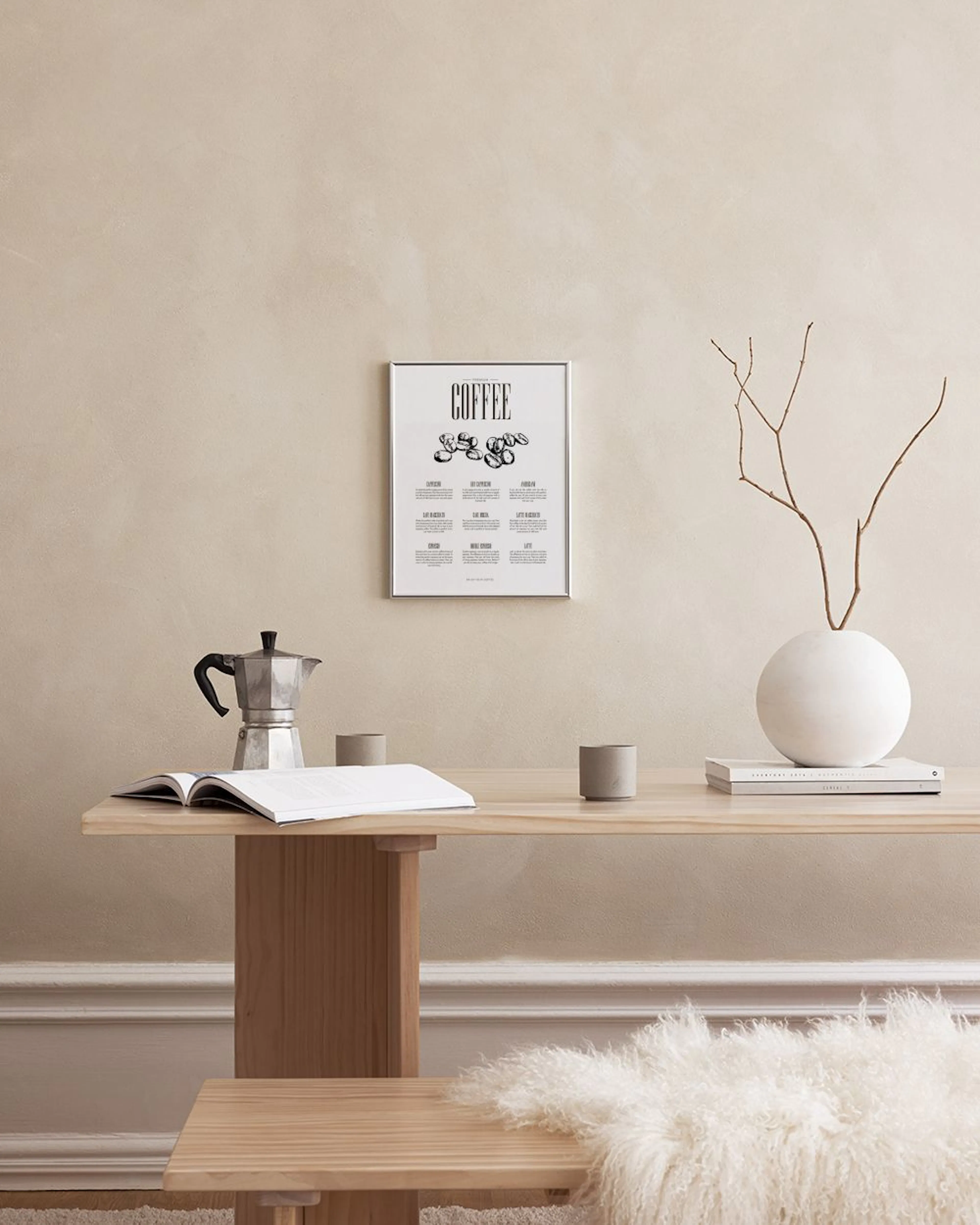 A coffee guide print with coffee beans and drink types, displayed on a white marble surface with a plant and accessories.