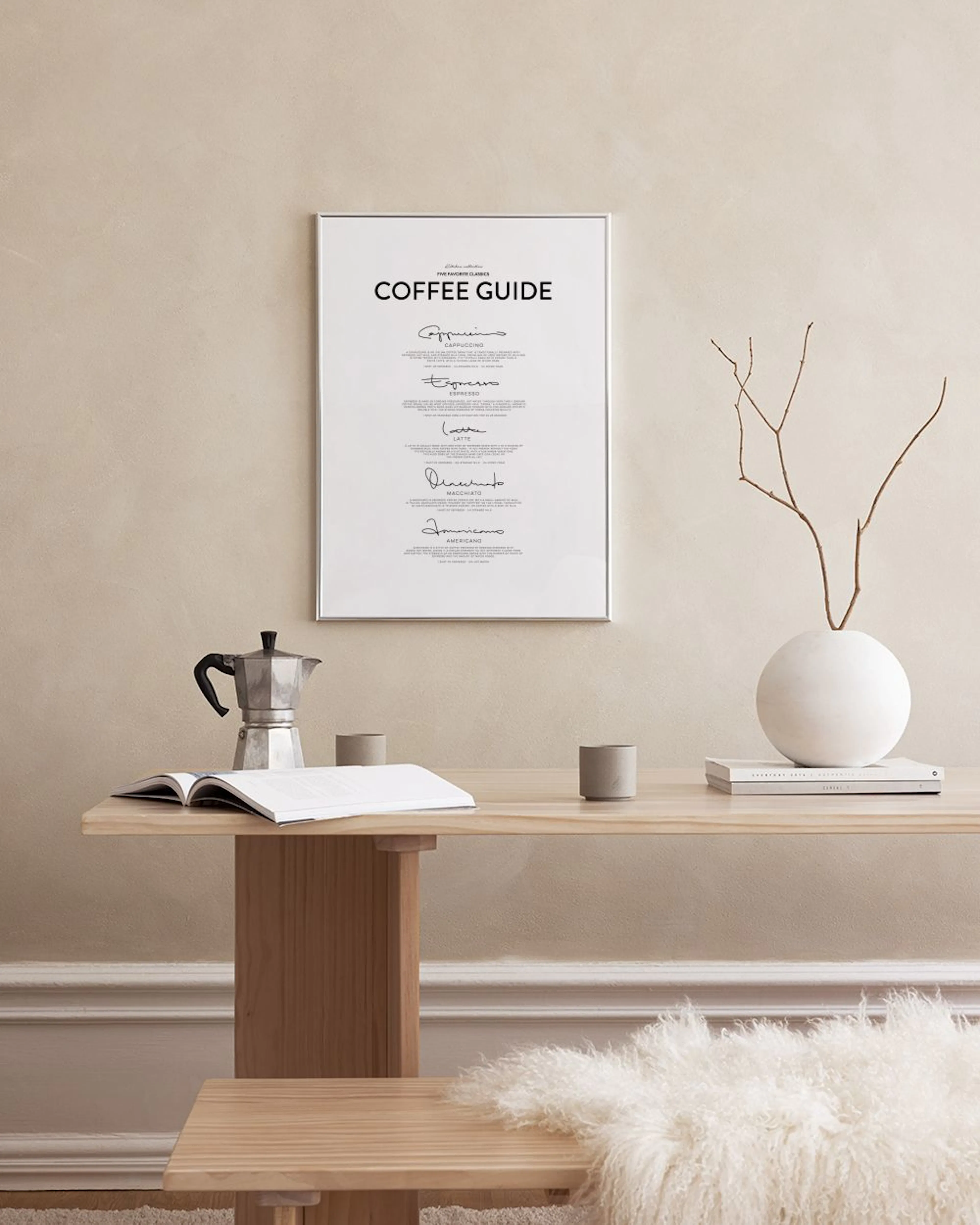Biely plagát Coffee Guide s čiernym písmom na mramorovej stene, vedľa čiernej vázy s rastlinou.