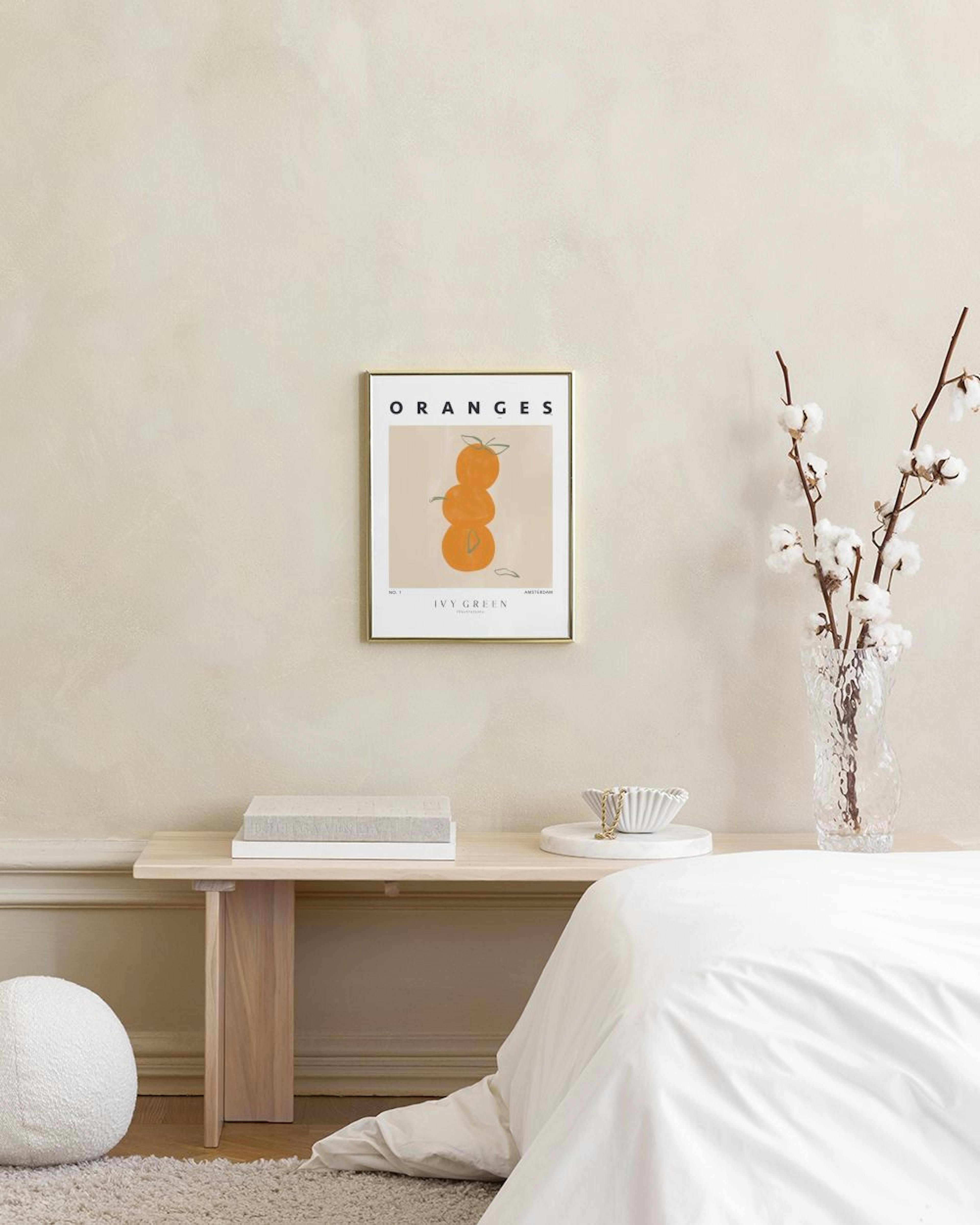 Poster con tre arance stilizzate arancioni e foglie verdi su sfondo beige, appeso sopra un tavolo in legno con bicchiere e vaso.
