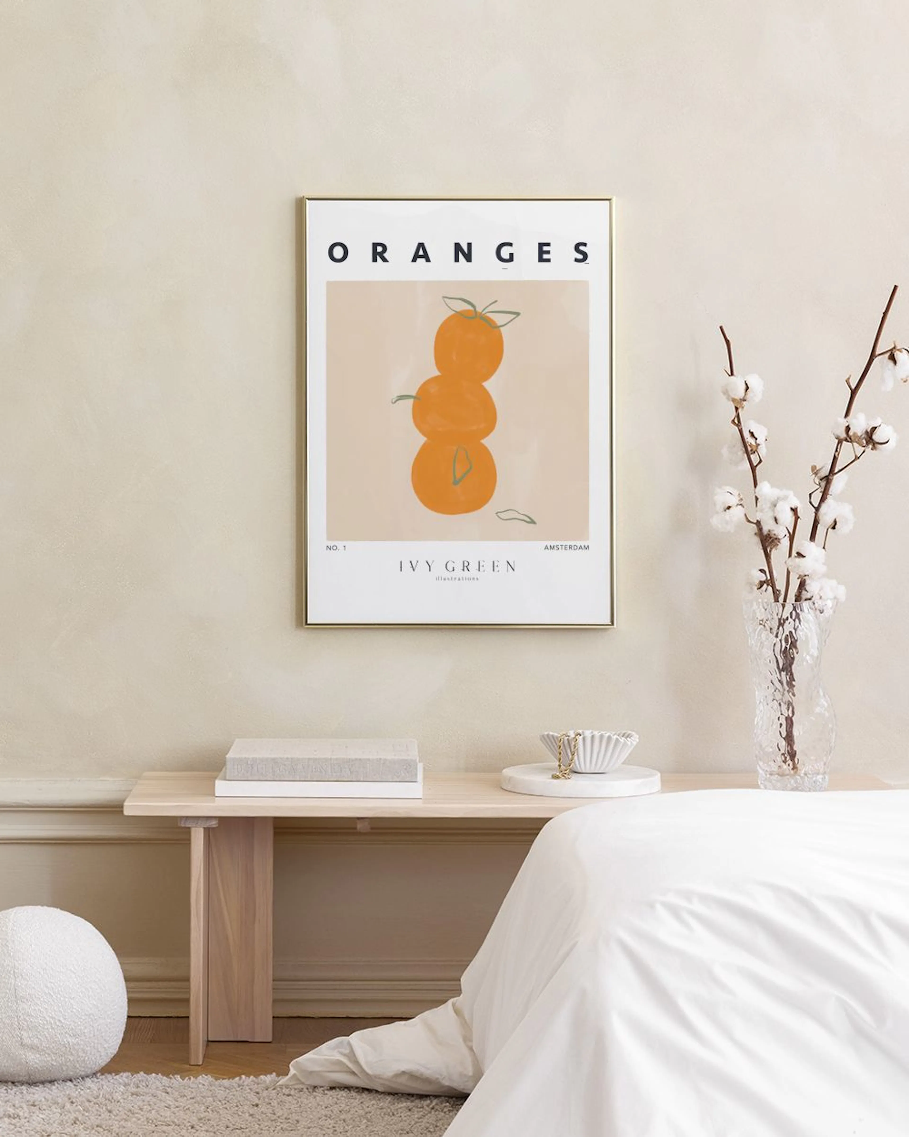 A minimalist print of three stacked oranges with green leaves on a light background, hanging above a wooden table with a glass, 