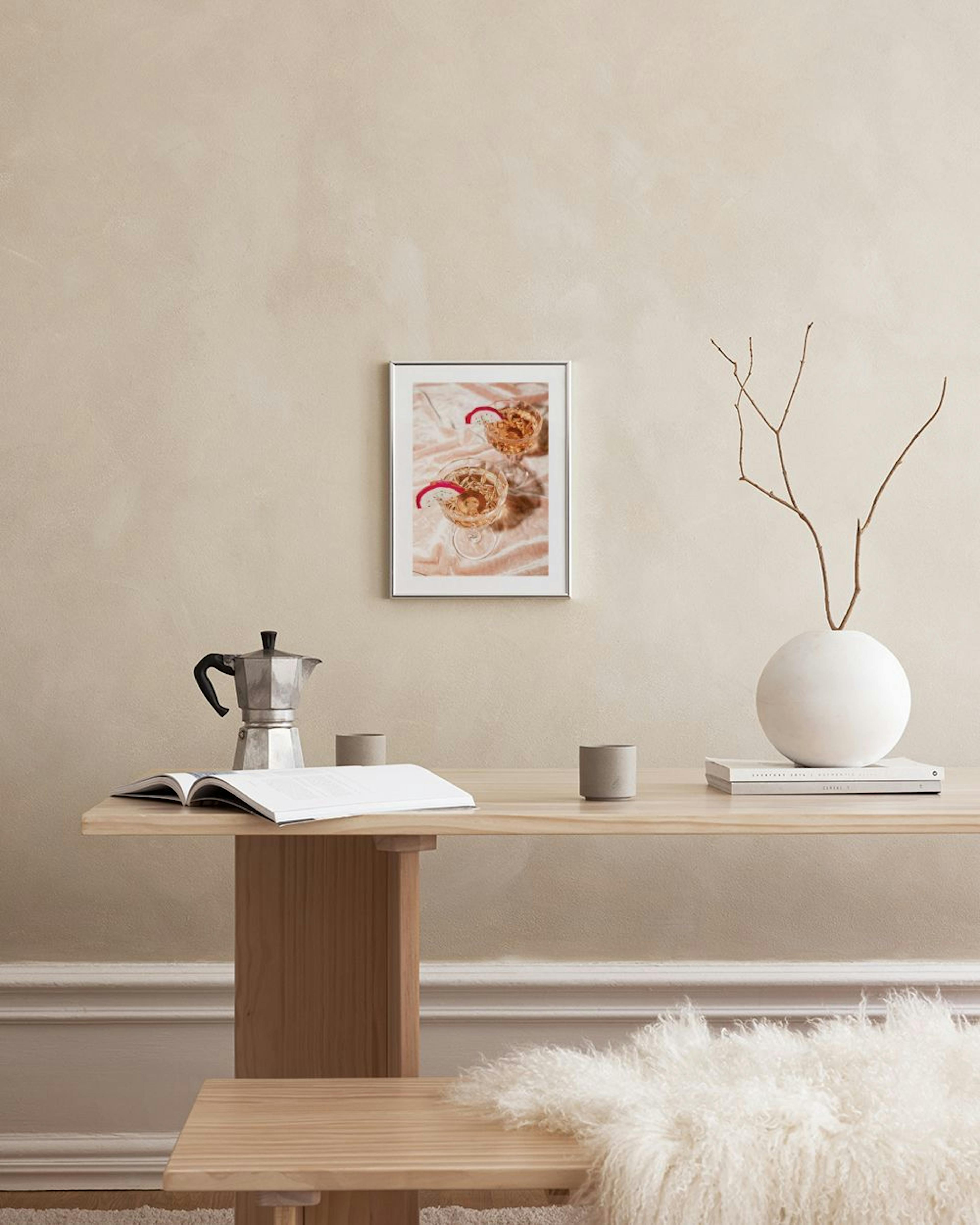 Ein Poster mit zwei Cocktailgläsern mit Drachenfrucht, an einer beigen Wand über einem Beistelltisch und Sessel.