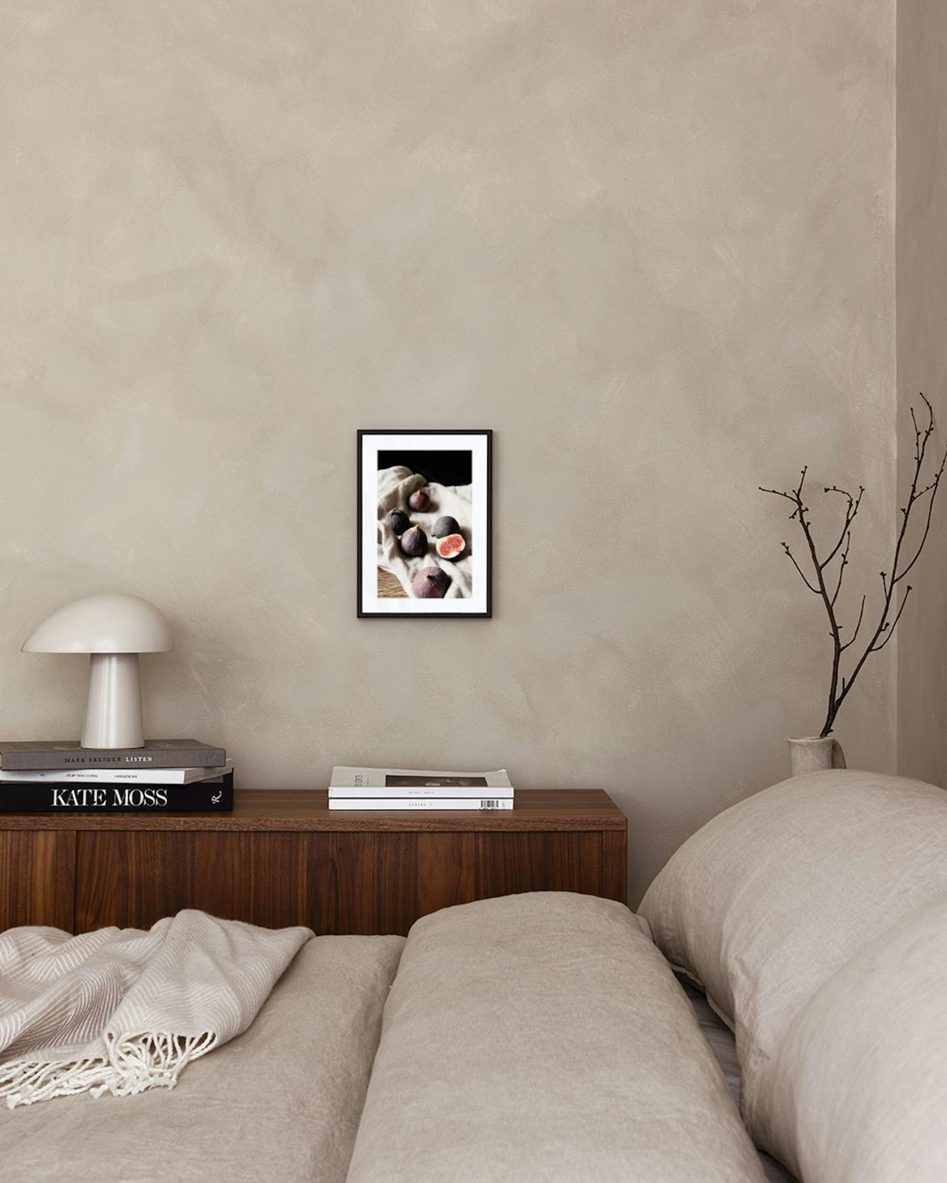 A print of several figs, one cut open to reveal red flesh, on a light linen cloth, hanging above a light armchair.
