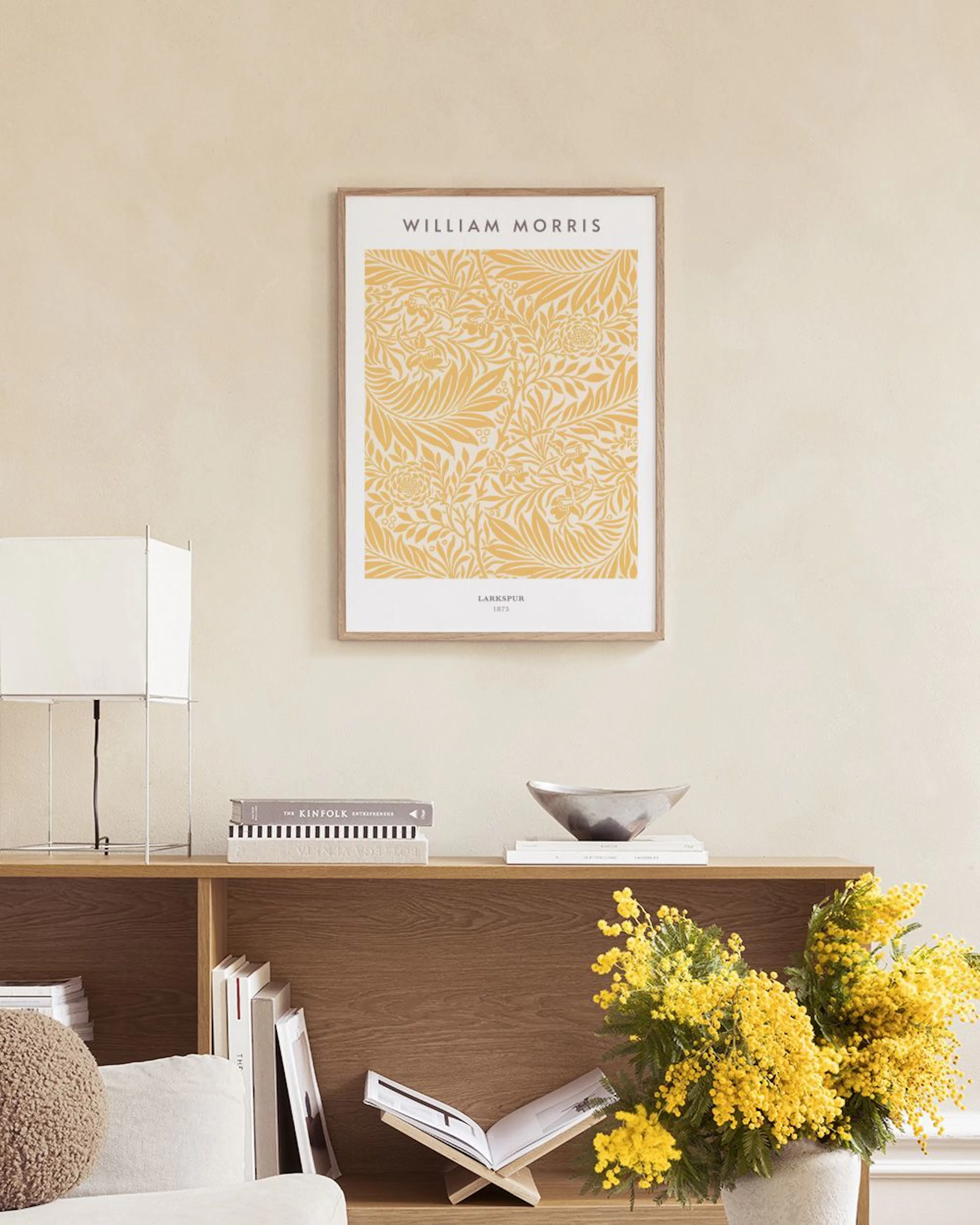 A William Morris print featuring yellow botanical patterns on a light background, hanging above a side table with a vase and can