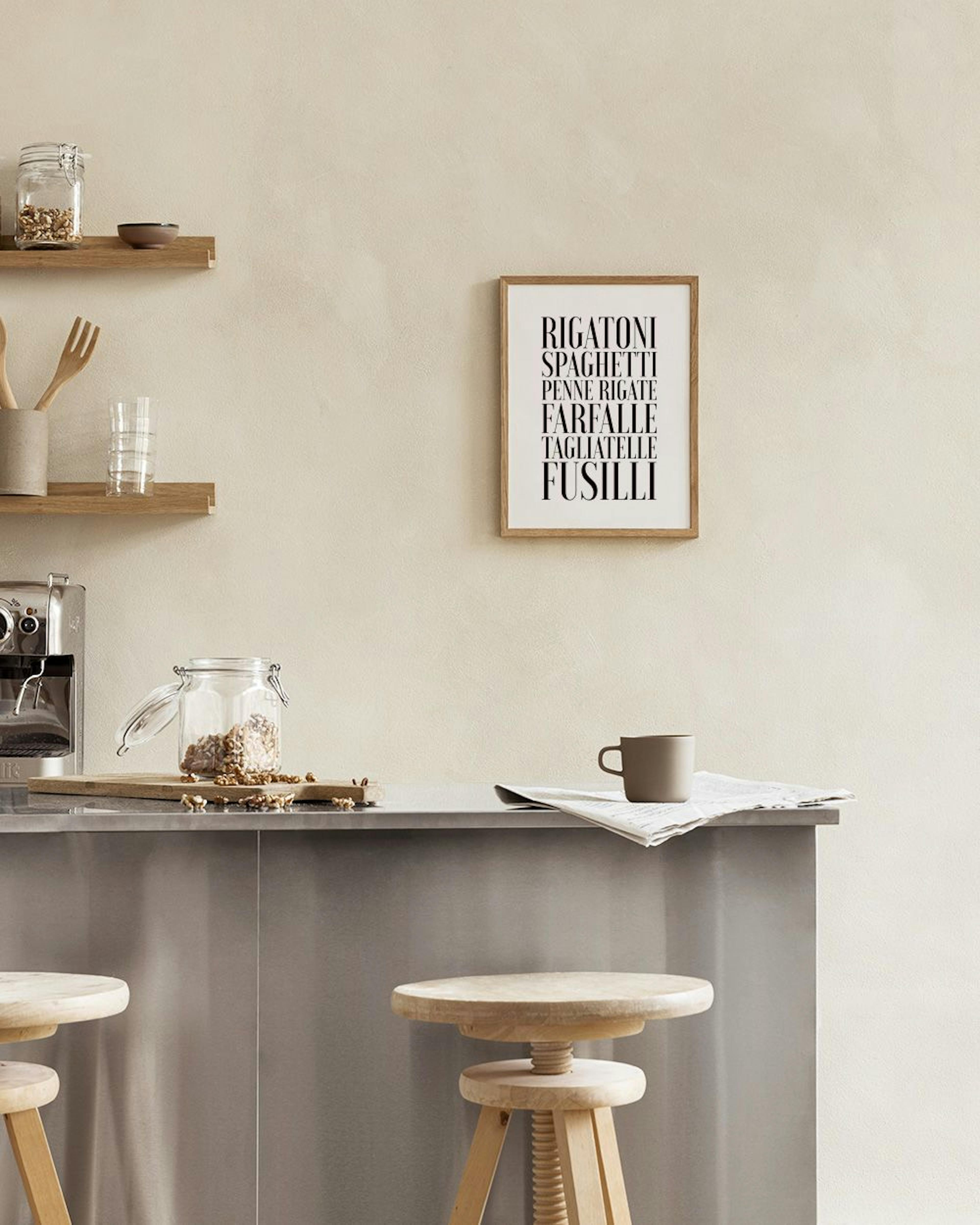 A print with various pasta names in bold black font, hanging above a white cupboard with mugs and bottles.