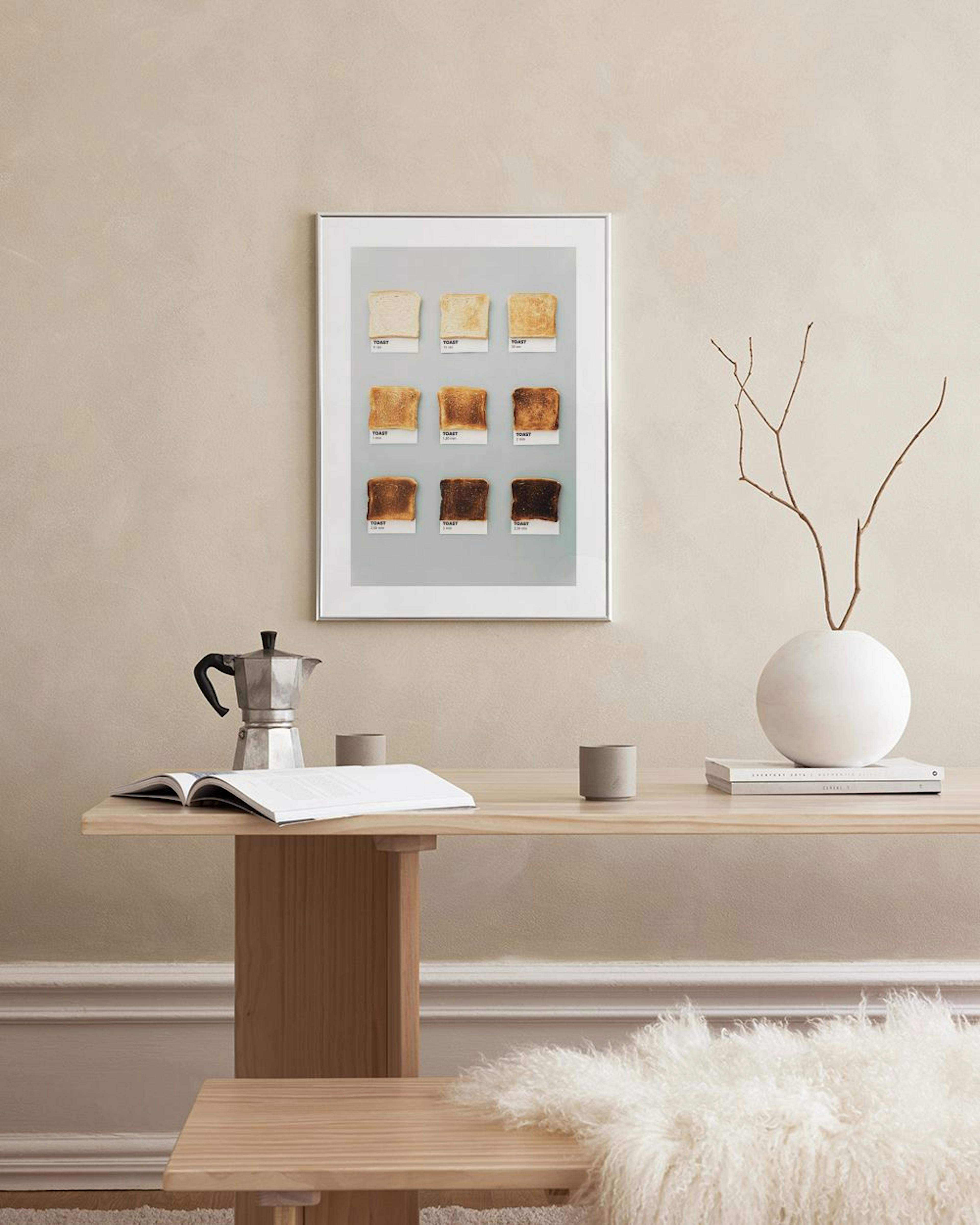 A print of nine toast slices, each with a different shade of browning, hanging on a white wall above a dining table.