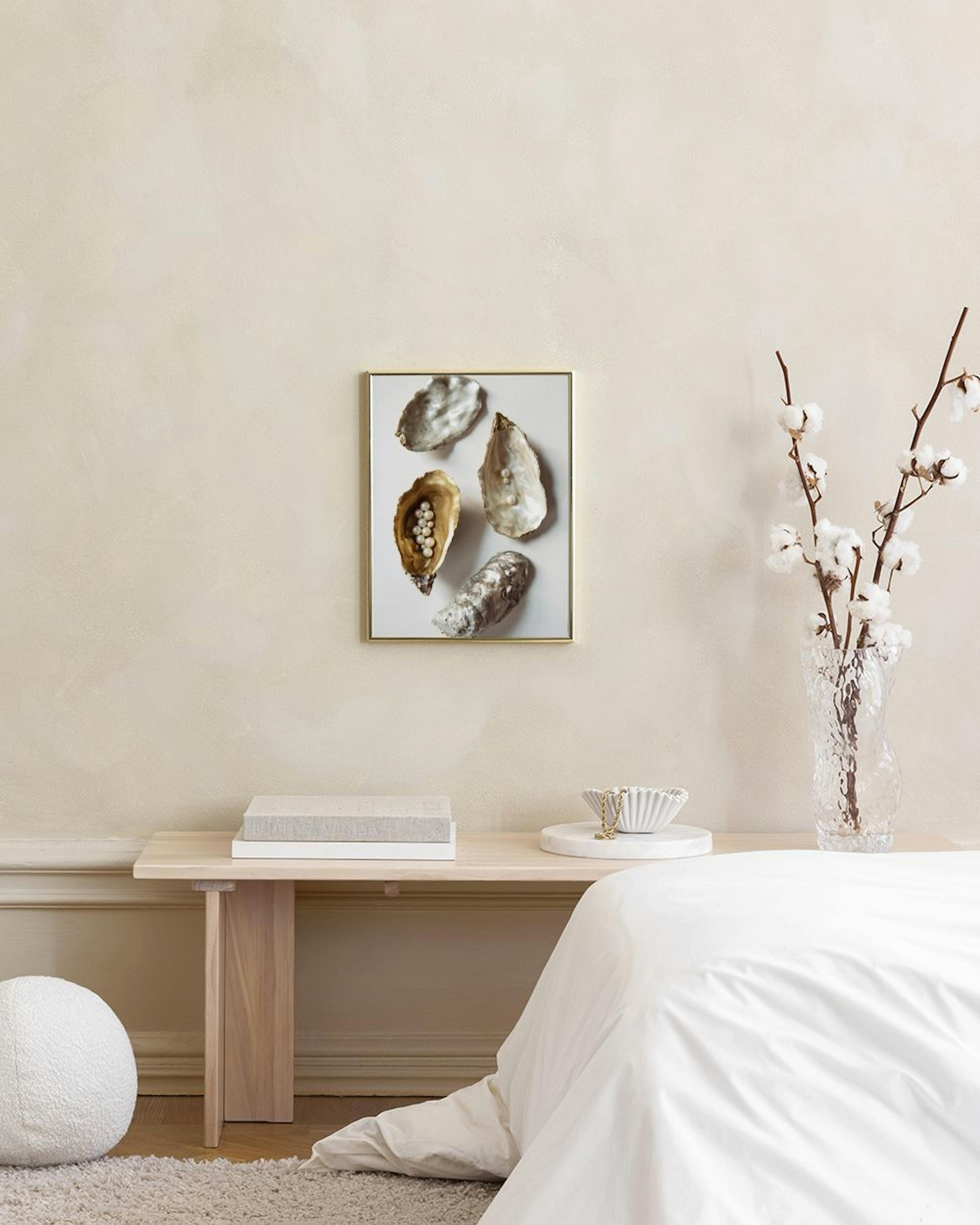 Poster de ostras com pérolas em tons dourados e prateados, pendurado numa parede cinzenta acima de uma mesa lateral e cadeira av