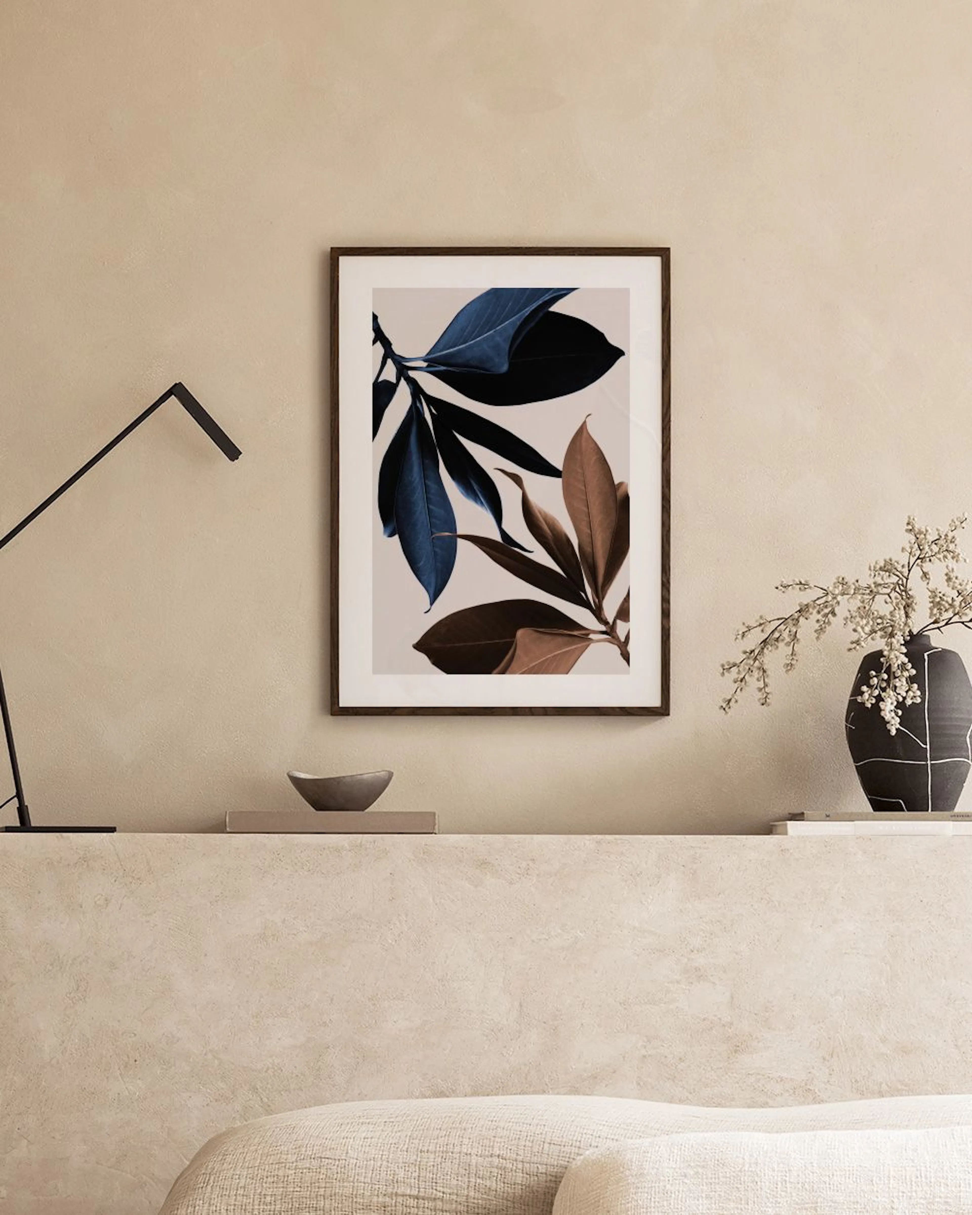 Poster met donkerblauwe en bruine bladeren, hangend boven een nachtkastje met kaars en naast een bed.
