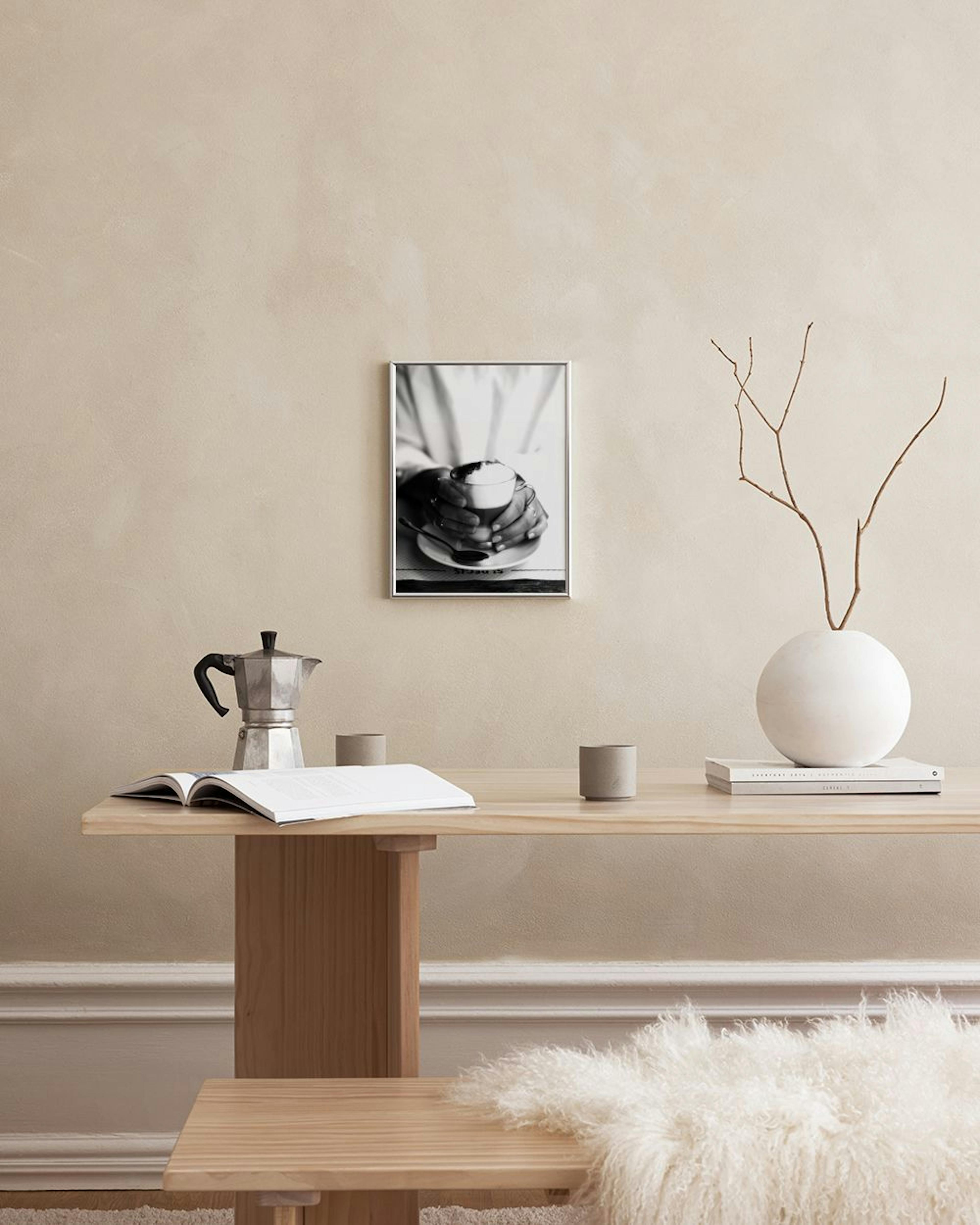 A black and white print of hands holding a coffee cup, displayed on a white windowsill with a decorative bowl.
