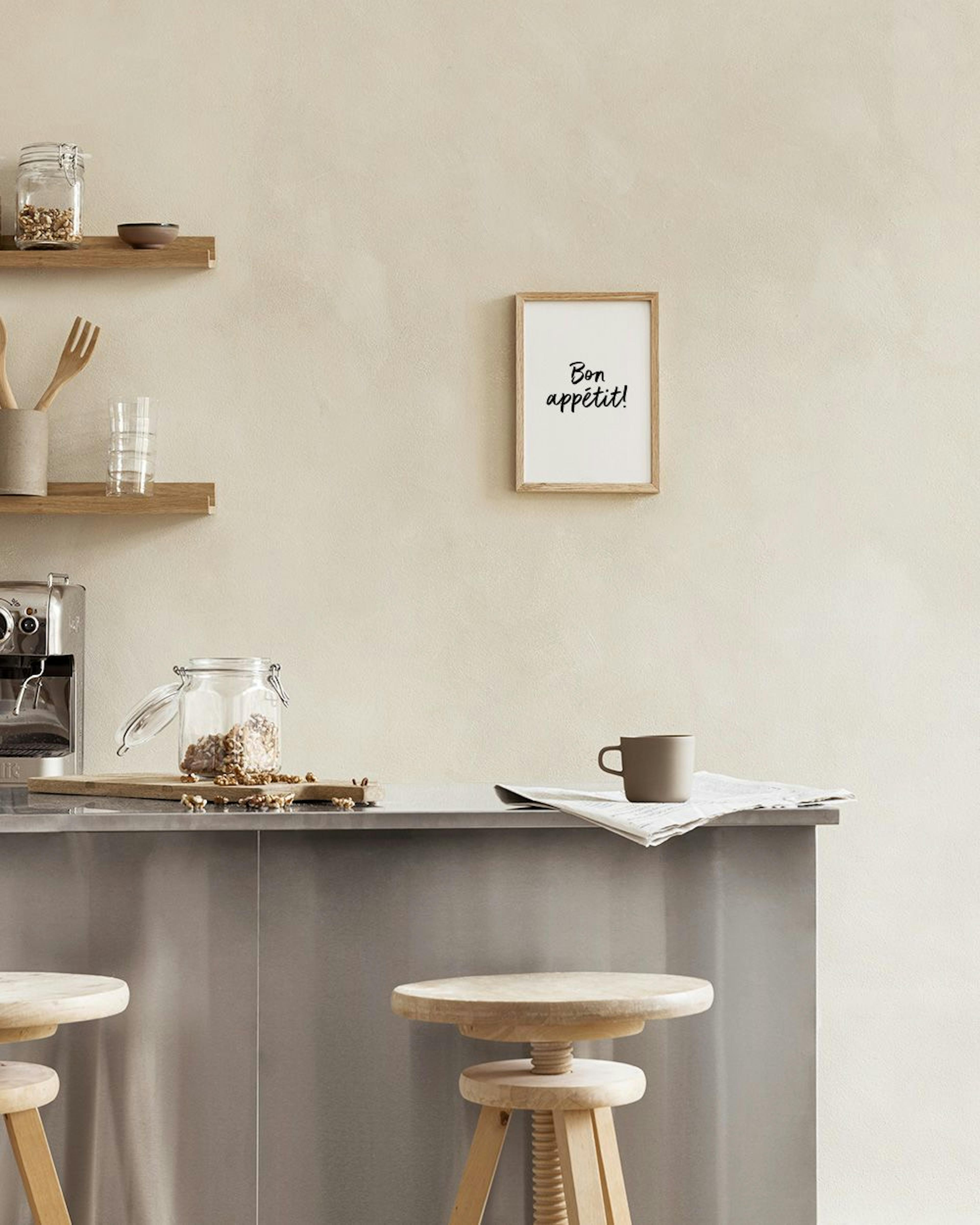 Een poster met de tekst Bon appétit! in zwarte letters, staand op een witte vensterbank met een theepot en boeken.