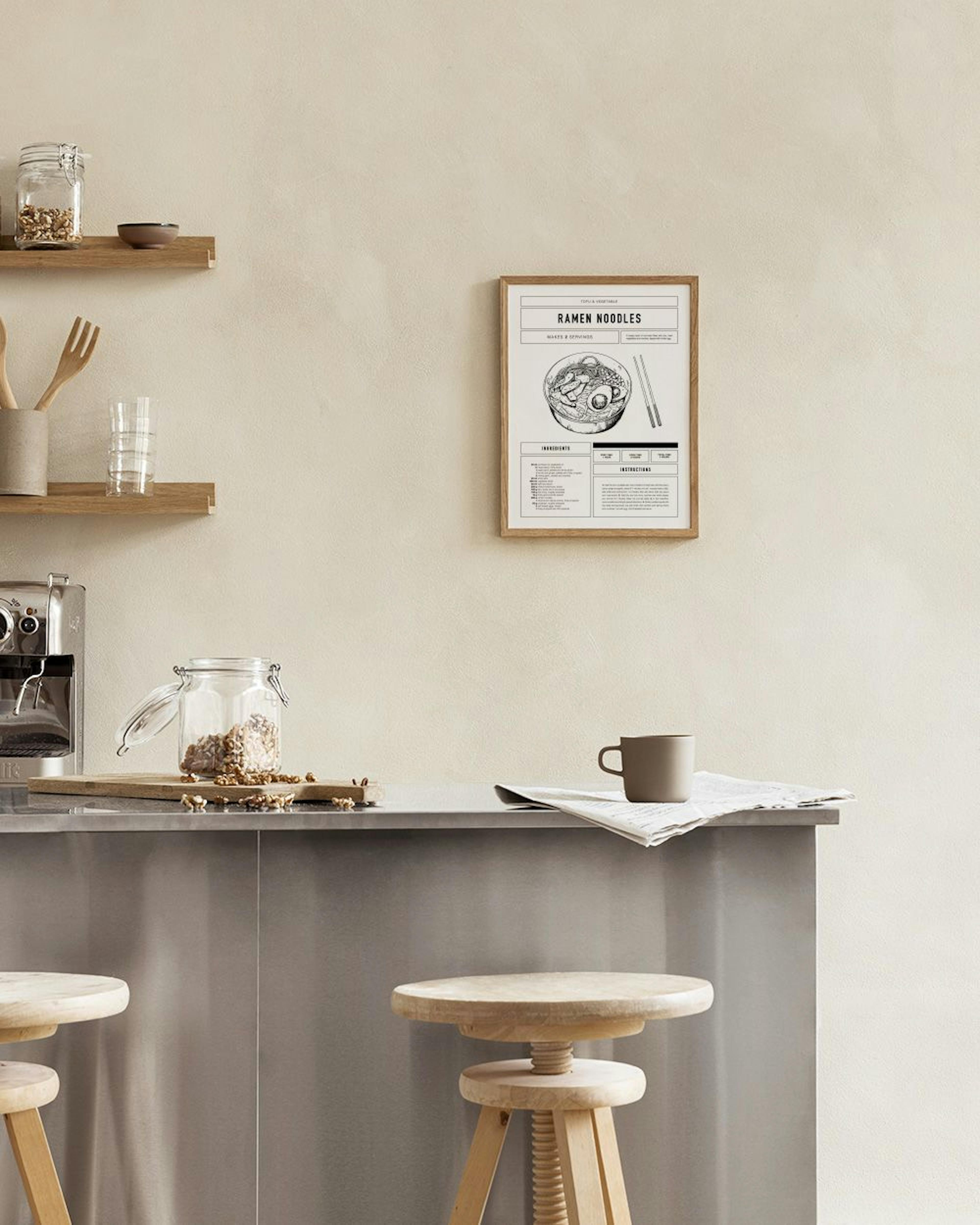 A black and white ramen noodles recipe print hanging on a white wall above a table with an open book and white candle.
