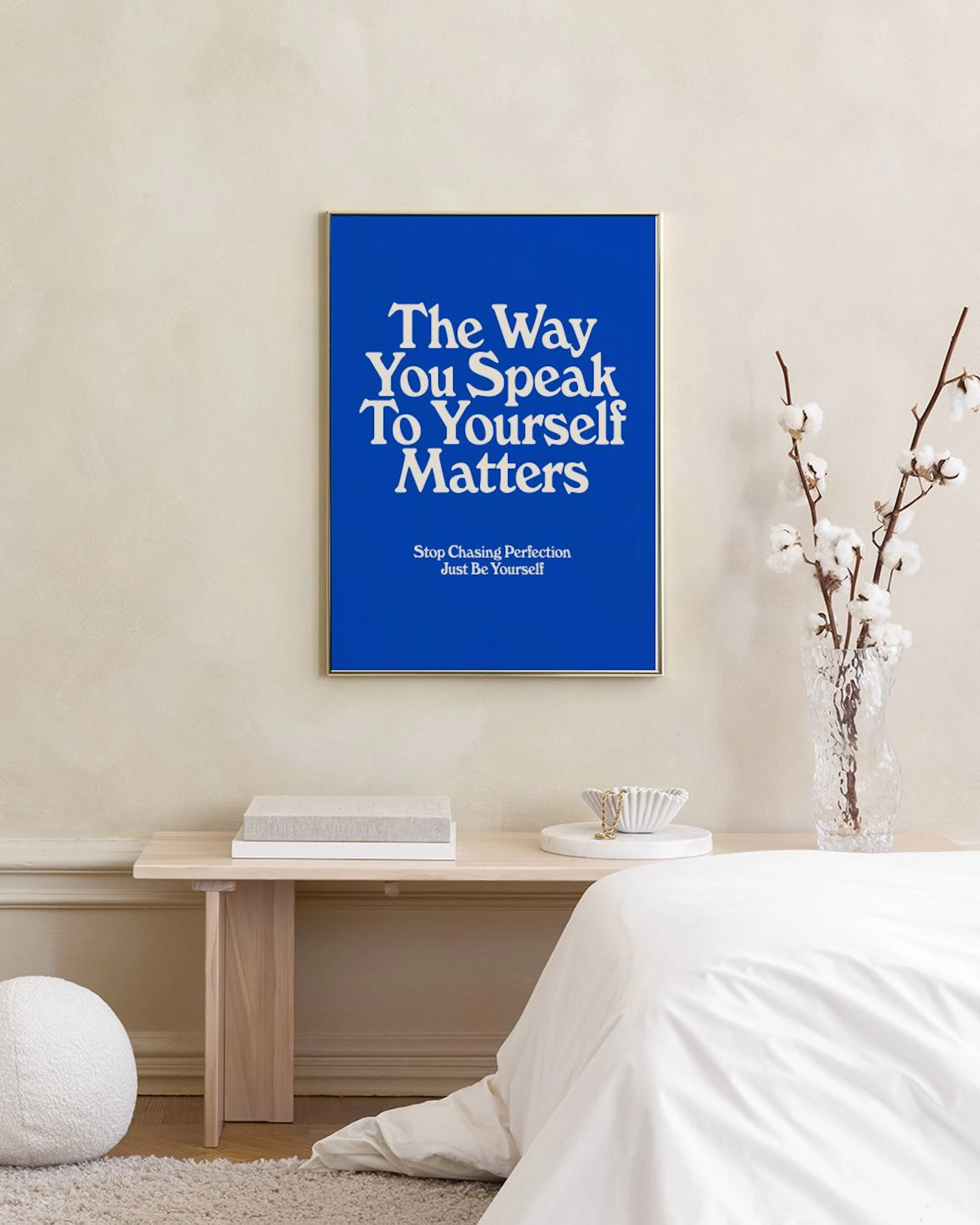 Een blauwe poster met witte tekst The Way You Speak To Yourself Matters, hangend boven een fauteuil met kussen.