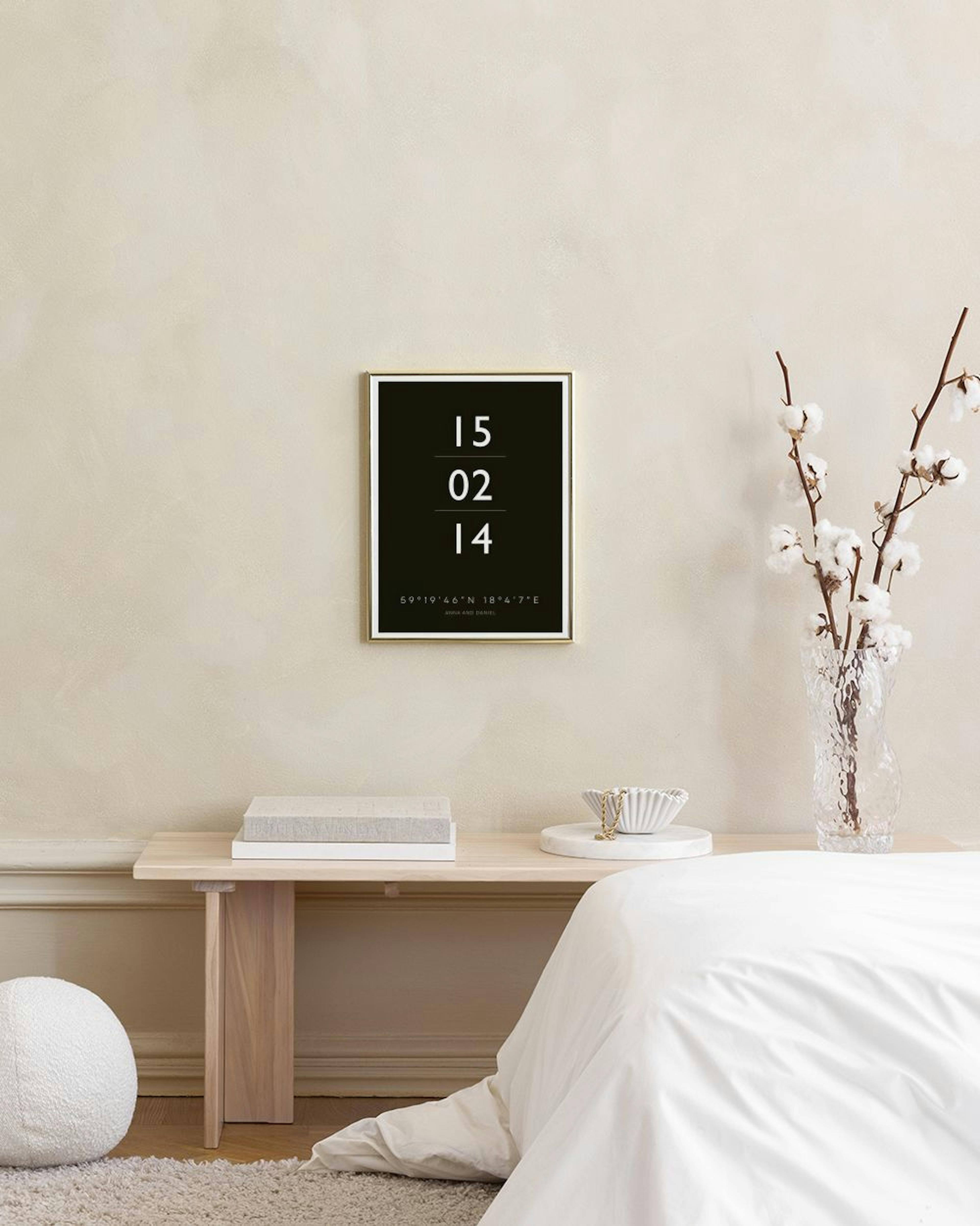 A personalised print with a date and coordinates on a black background, hanging above a bed with a nightstand and lamp.